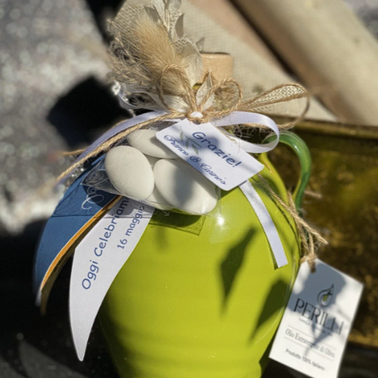 A green ceramic mug decorated with a ribbon, white stones, and a tag, placed outdoors with a blurred background.