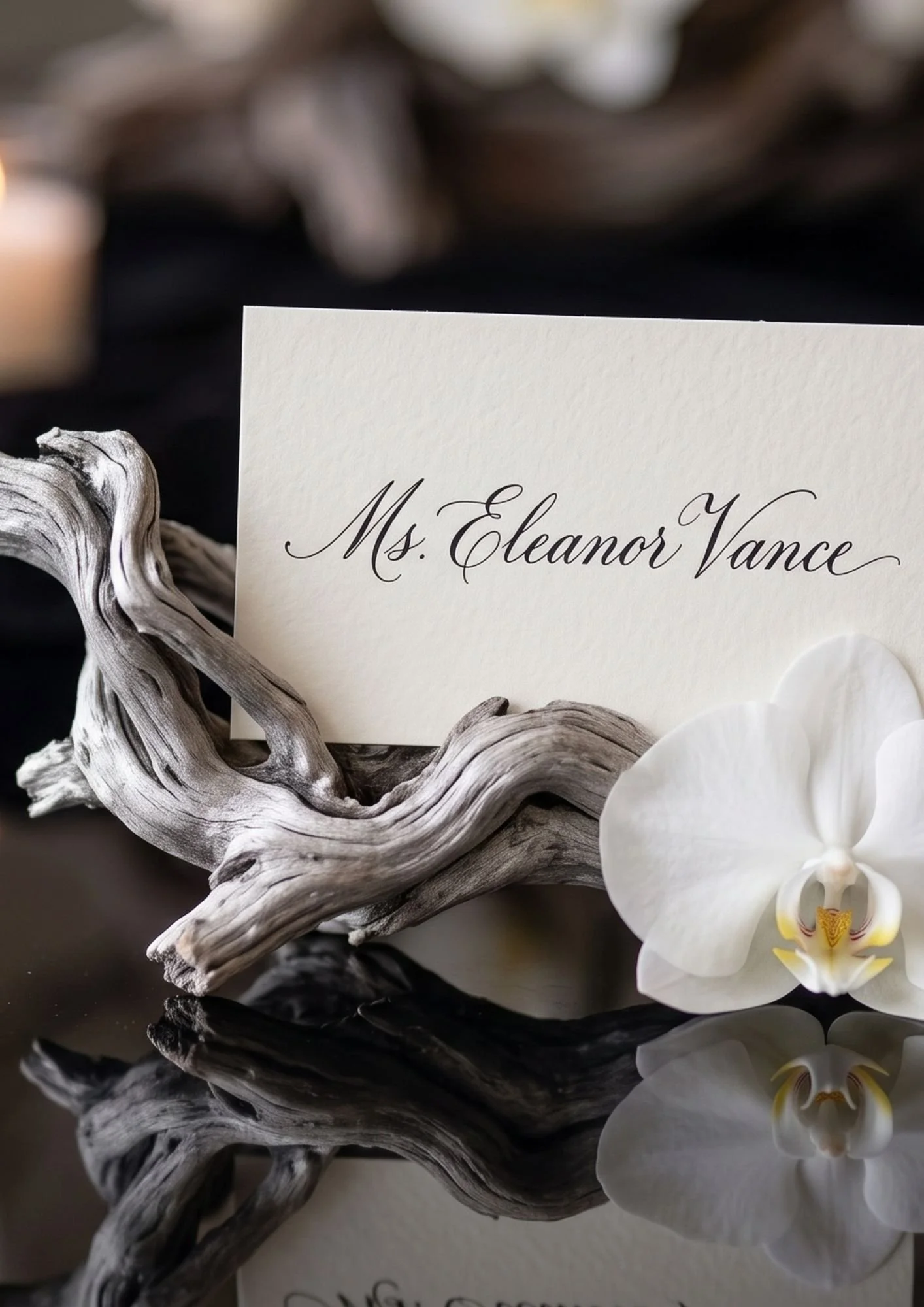 A white card with the name 'Ms. Eleanor Vance' in elegant script is surrounded by twisted driftwood and white orchid flowers, set on a black reflective surface.