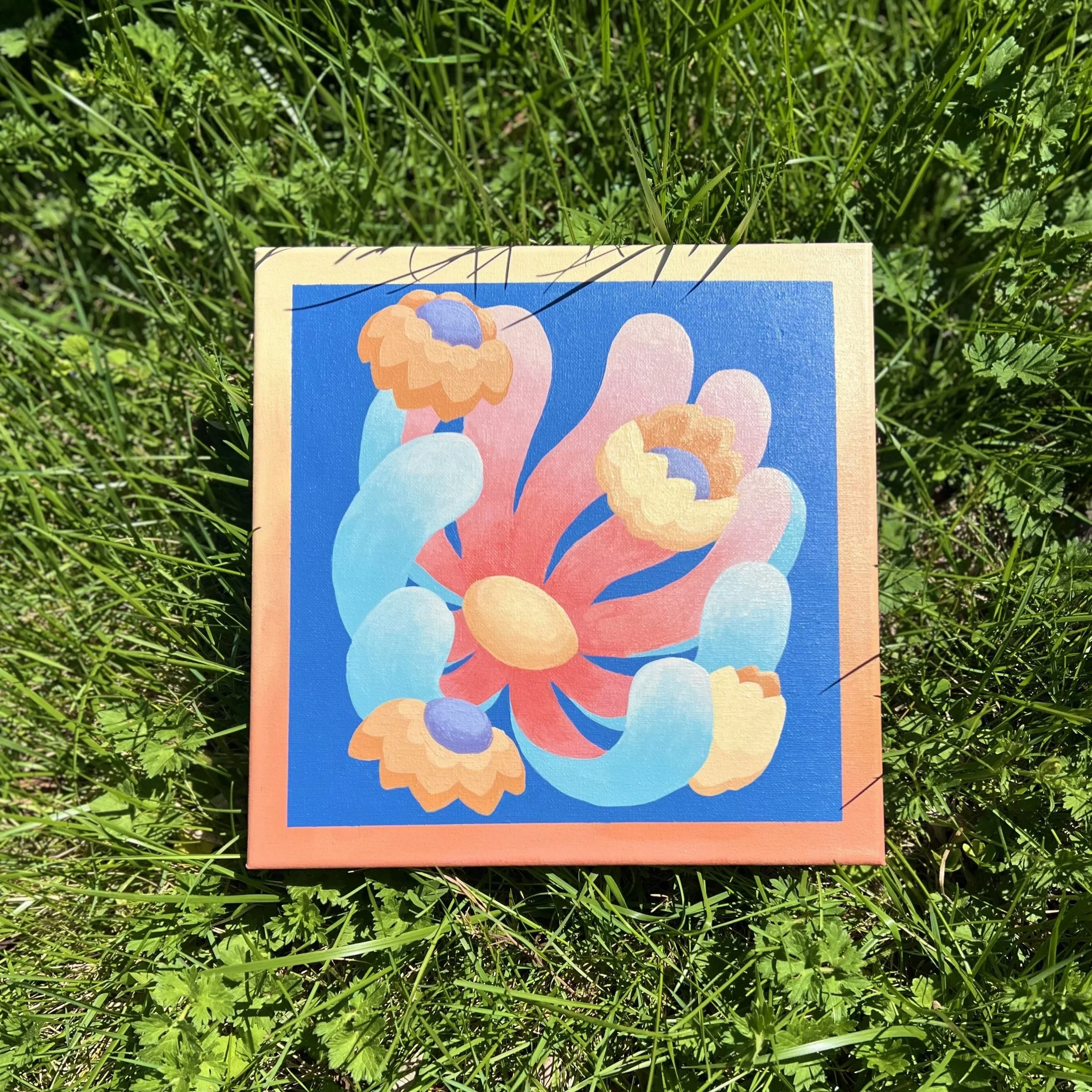 Close-up of a colorful painting of abstract clouds and sky, lying on green grass.