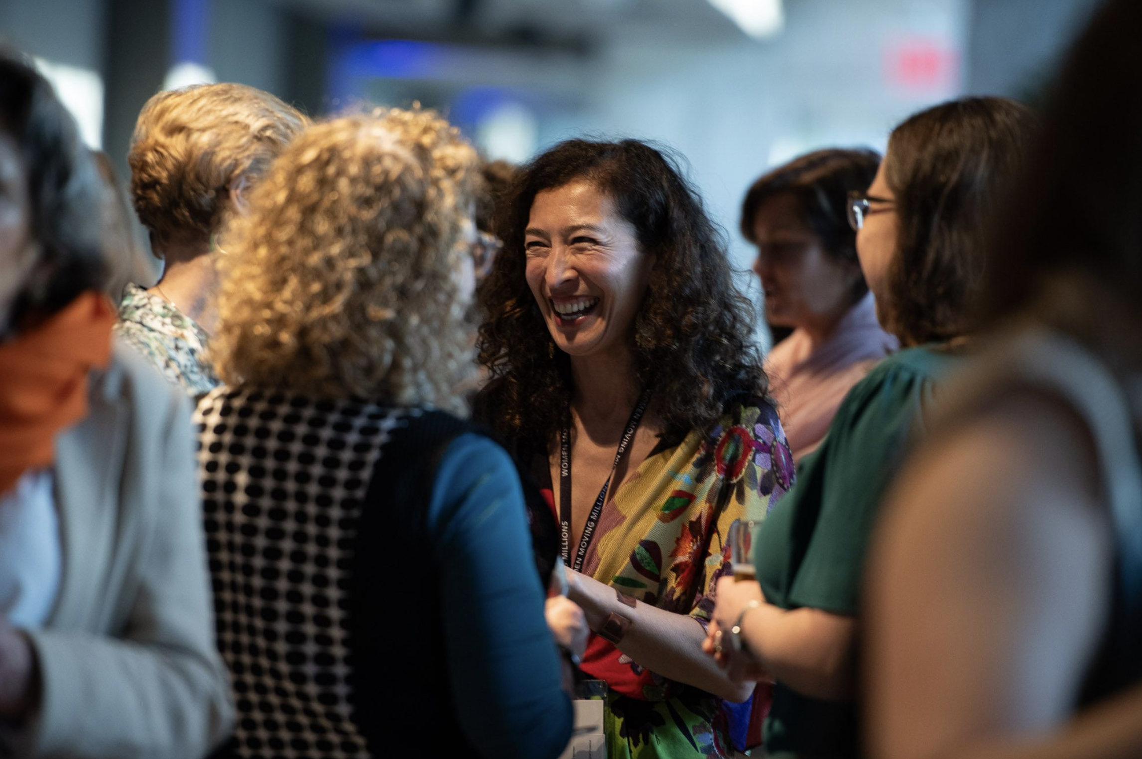 A group of women engaging in conversation at an indoor event, with one woman smiling warmly at others.