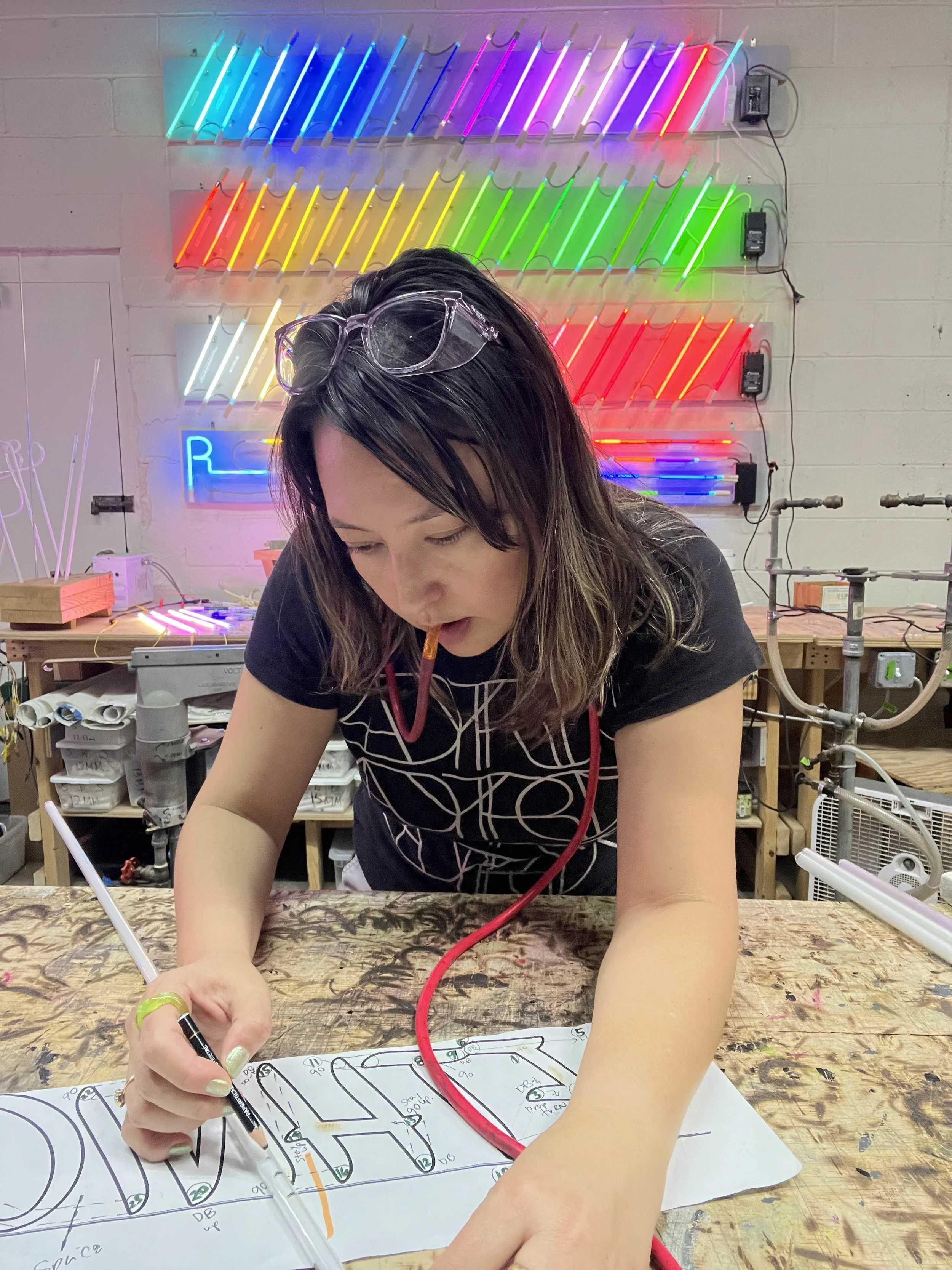 A woman with glasses on her head is drawing a pattern on a piece of paper on a wooden table.