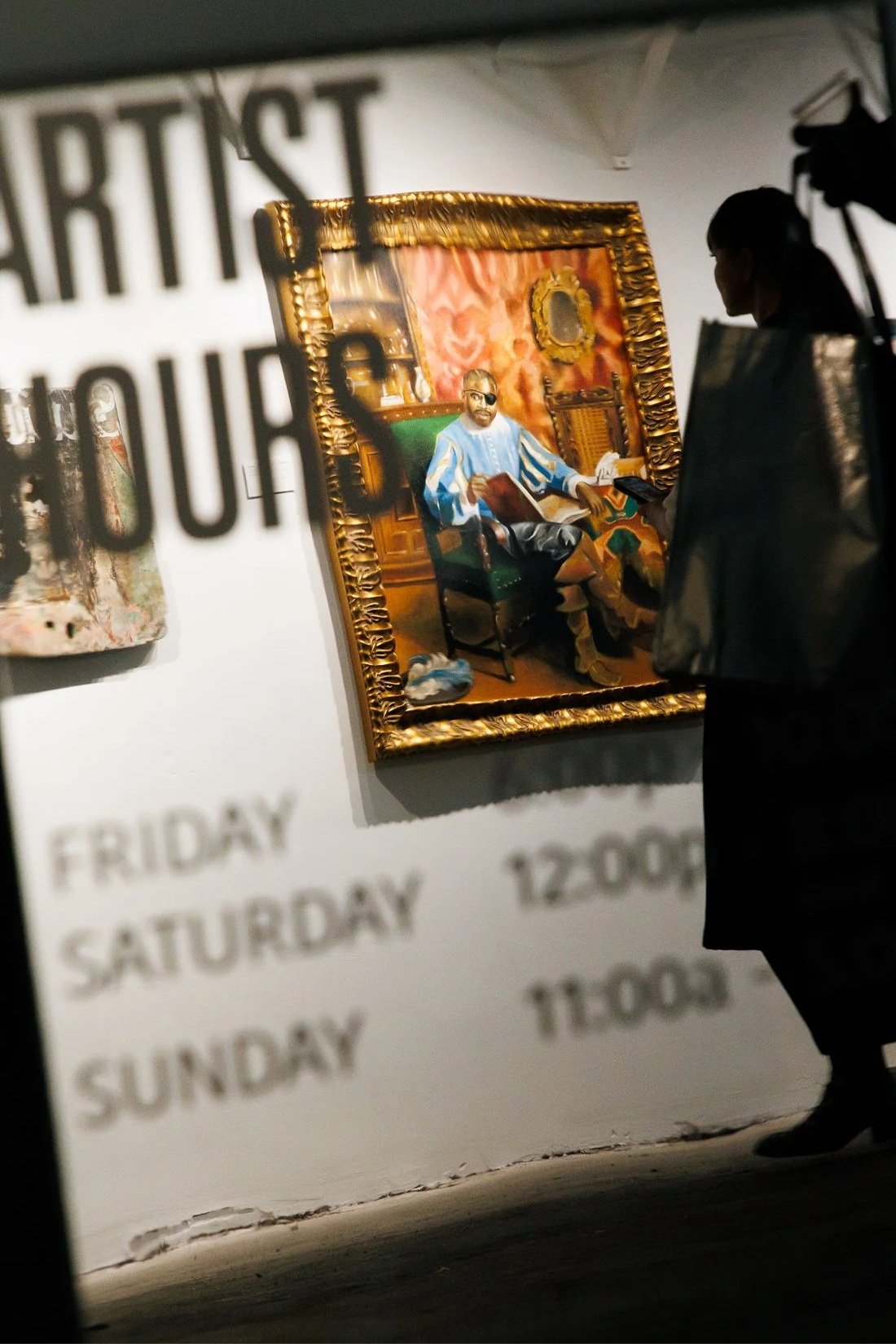 An art gallery with a portrait of a man sitting in a chair, wearing glasses and a blue and gold striped outfit, inside an ornate gold frame. The scene is seen through a glass wall with partial blurred words listing days of the week and times.