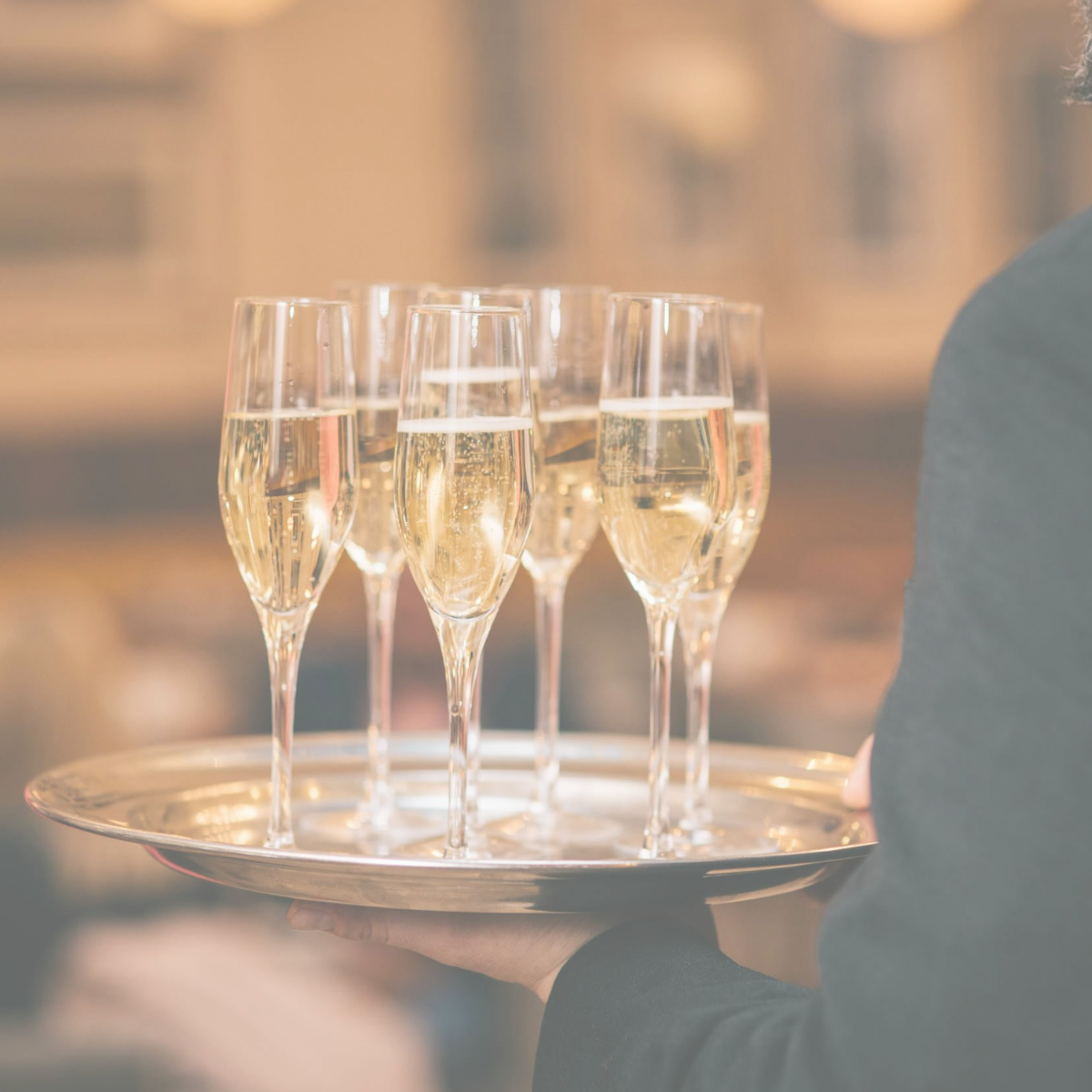 A waiter holding a tray with several glasses of champagne in a close-up shot at a celebration or event.