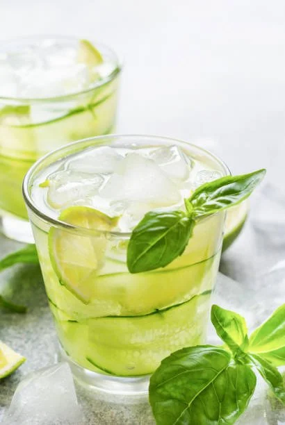 Verre de cocktail au basilic, citron, et glaçons, avec feuilles de basilic frais.