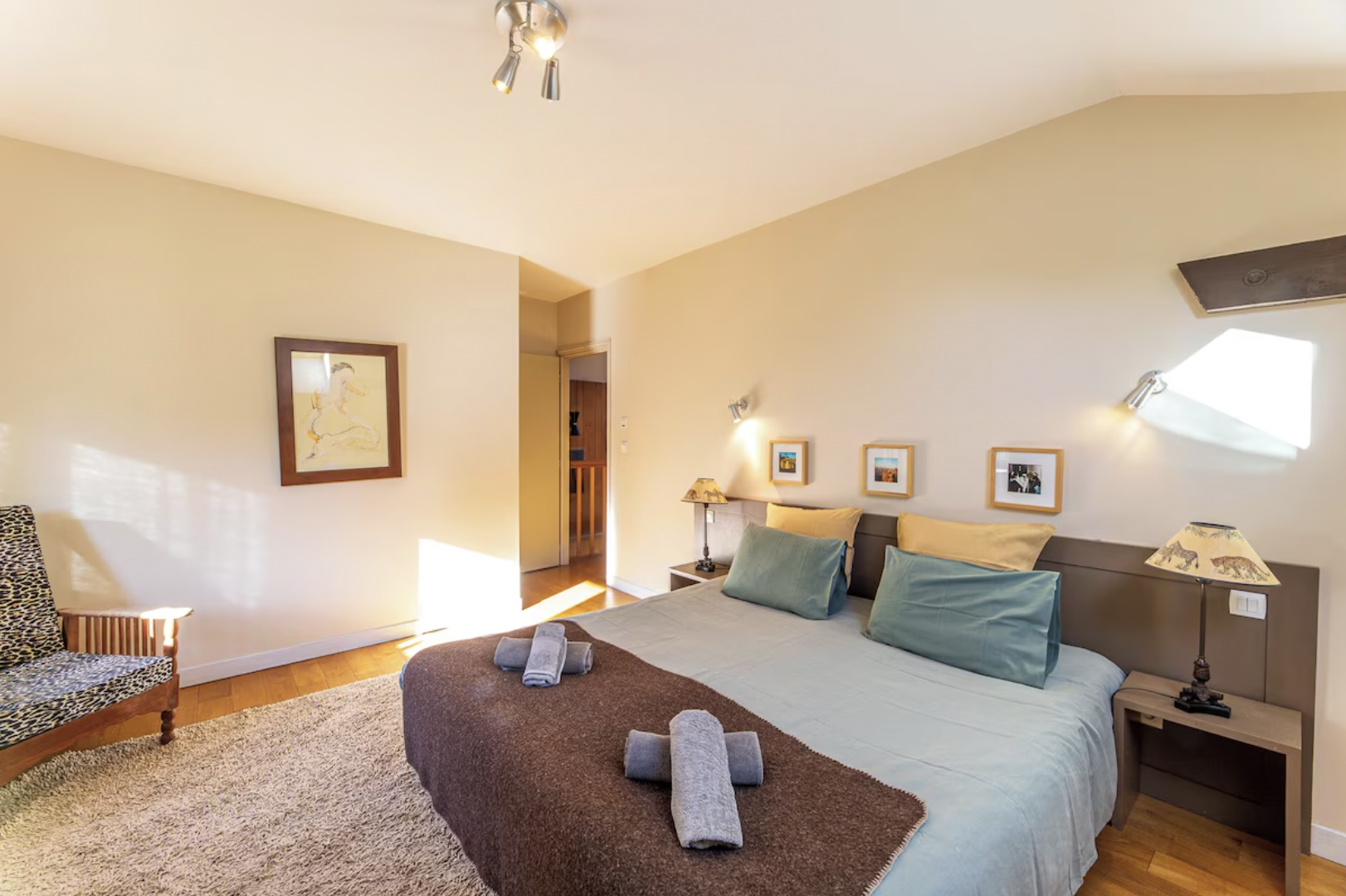 Chambre avec un lit double, coussins verts et jaunes, lampes de chevet avec abat-jours illustrés d'éléphants, tableau au mur, tapis beige, fenêtre avec lumière naturelle.