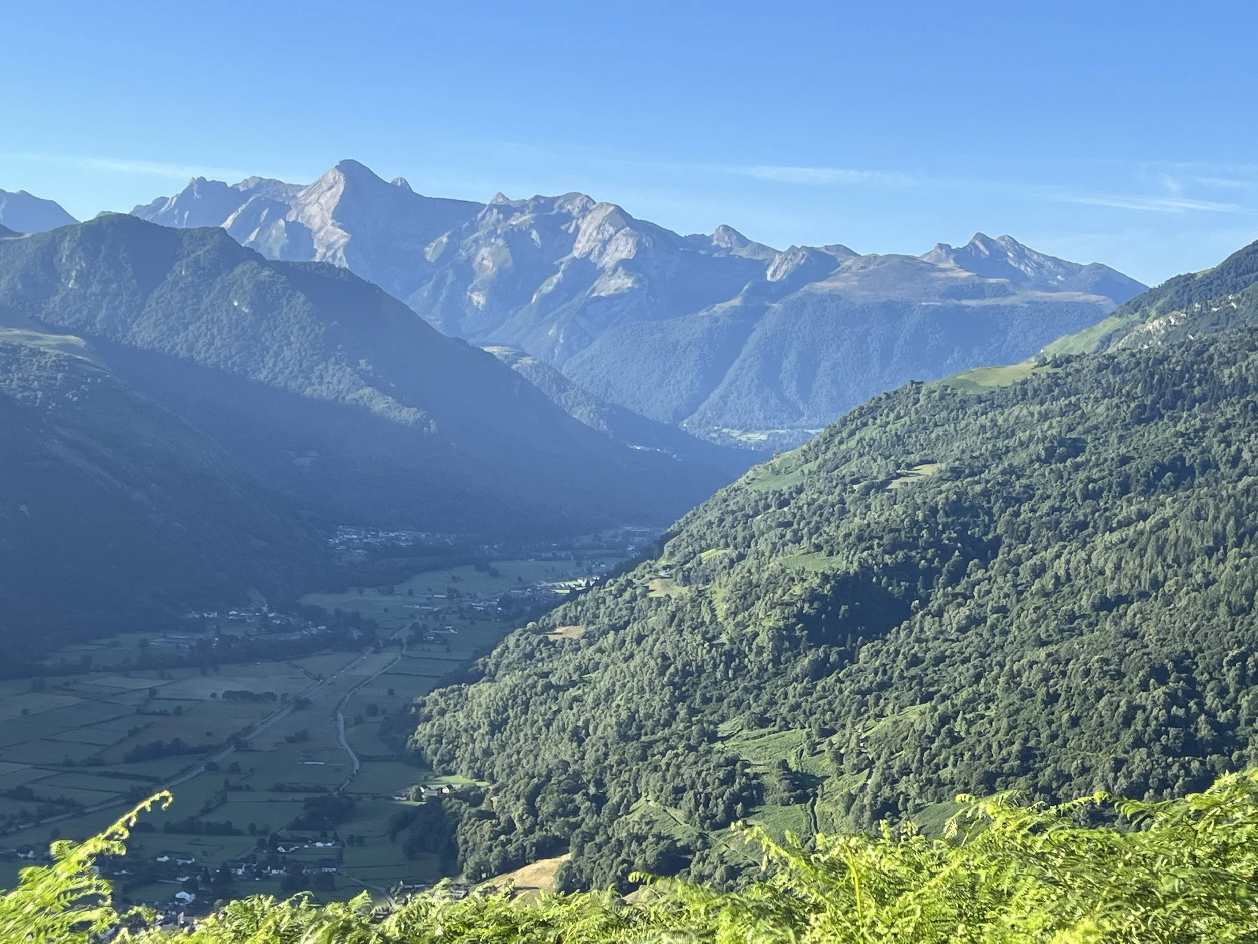 Paysage de montagnes verdoyantes avec vallée au centre, sous un ciel bleu clair.