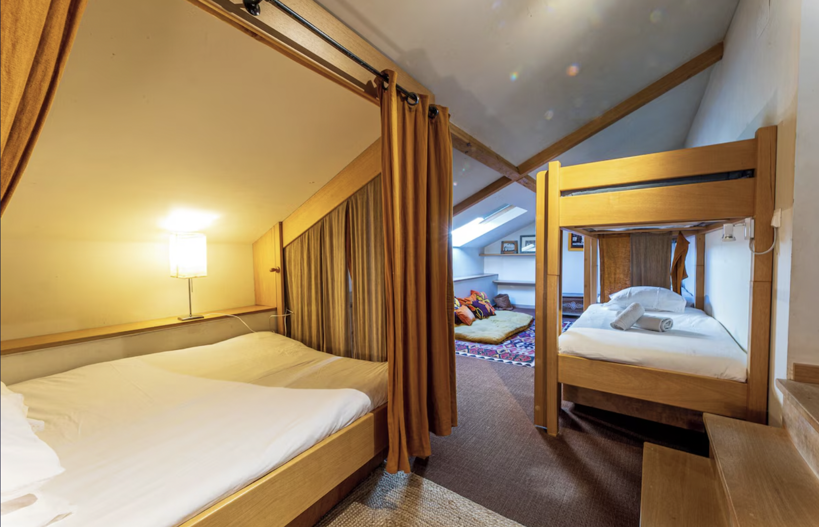 Chambre avec lits superposés, un lit double et un coin salon avec des coussins sur un tapis.
