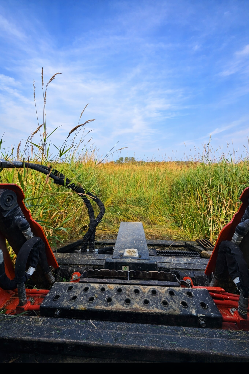 View from a farming machine on a grassy field under a partly cloudy blue sky.