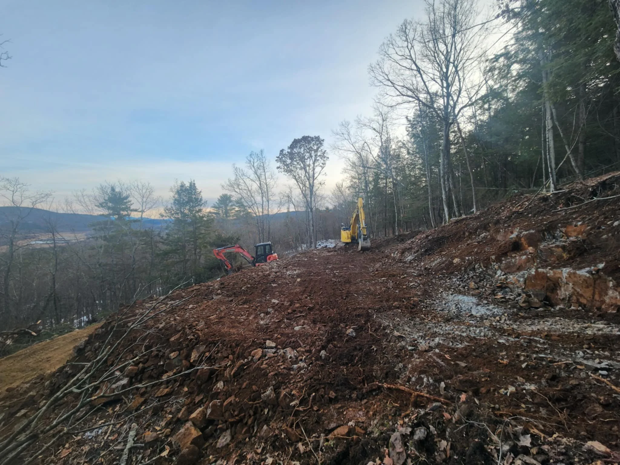 Construction site on a hillside with construction equipment clearing trees and earth.
