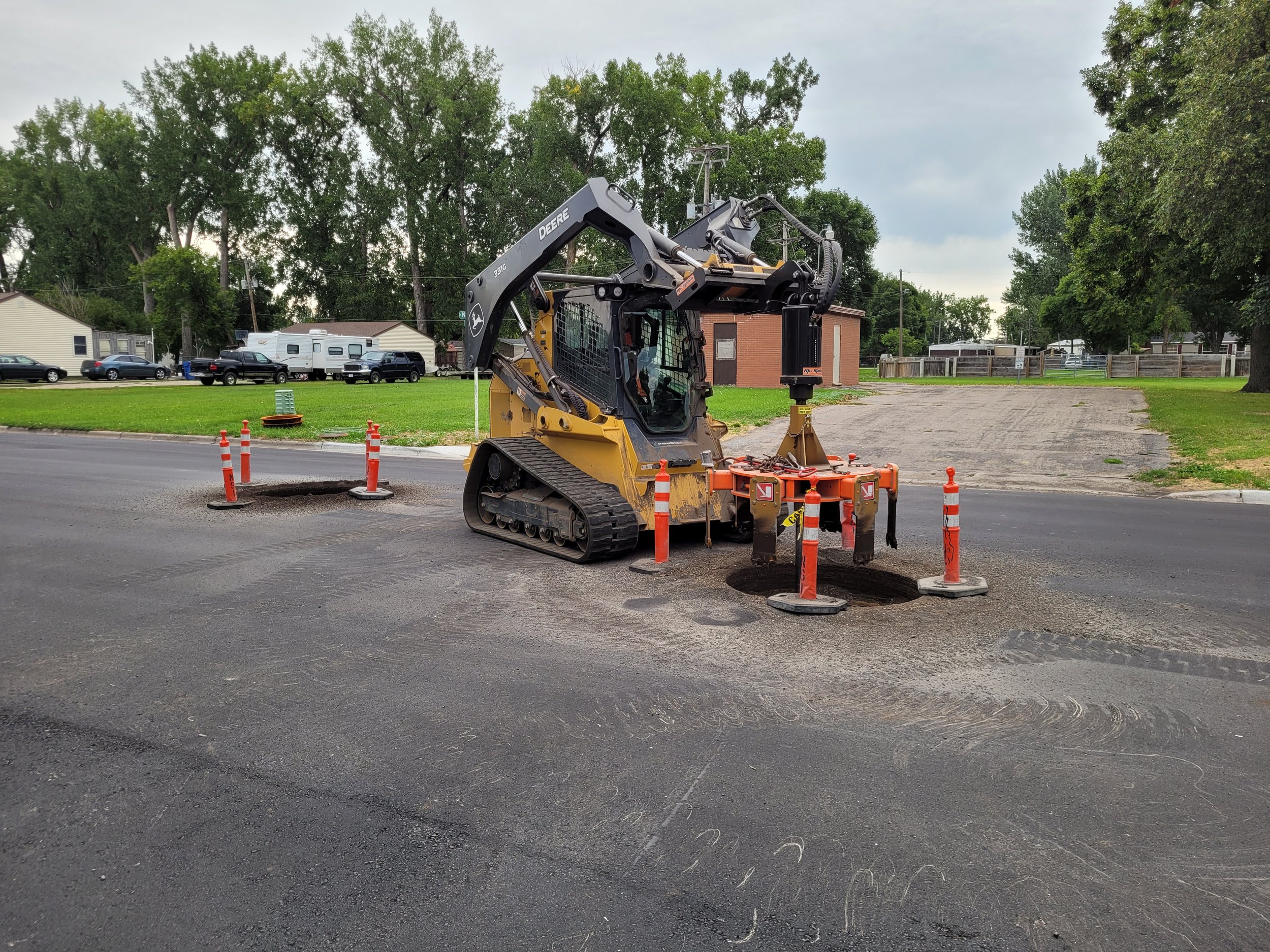 Construction site on a road with a small excavator and safety cones around dug holes.