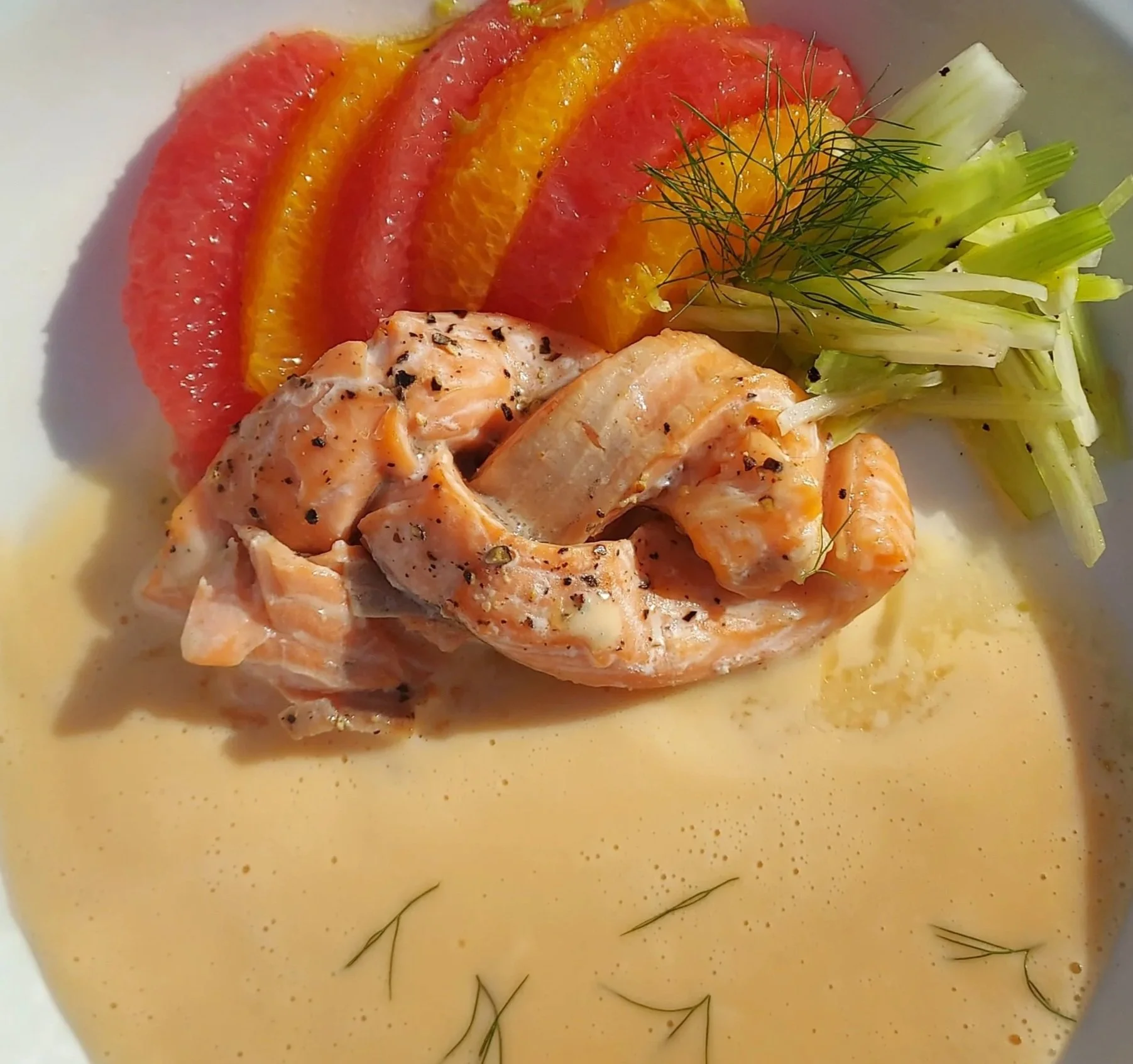 Sliced orange and grapefruit on a plate with a side of cooked salmon and fresh herbs.