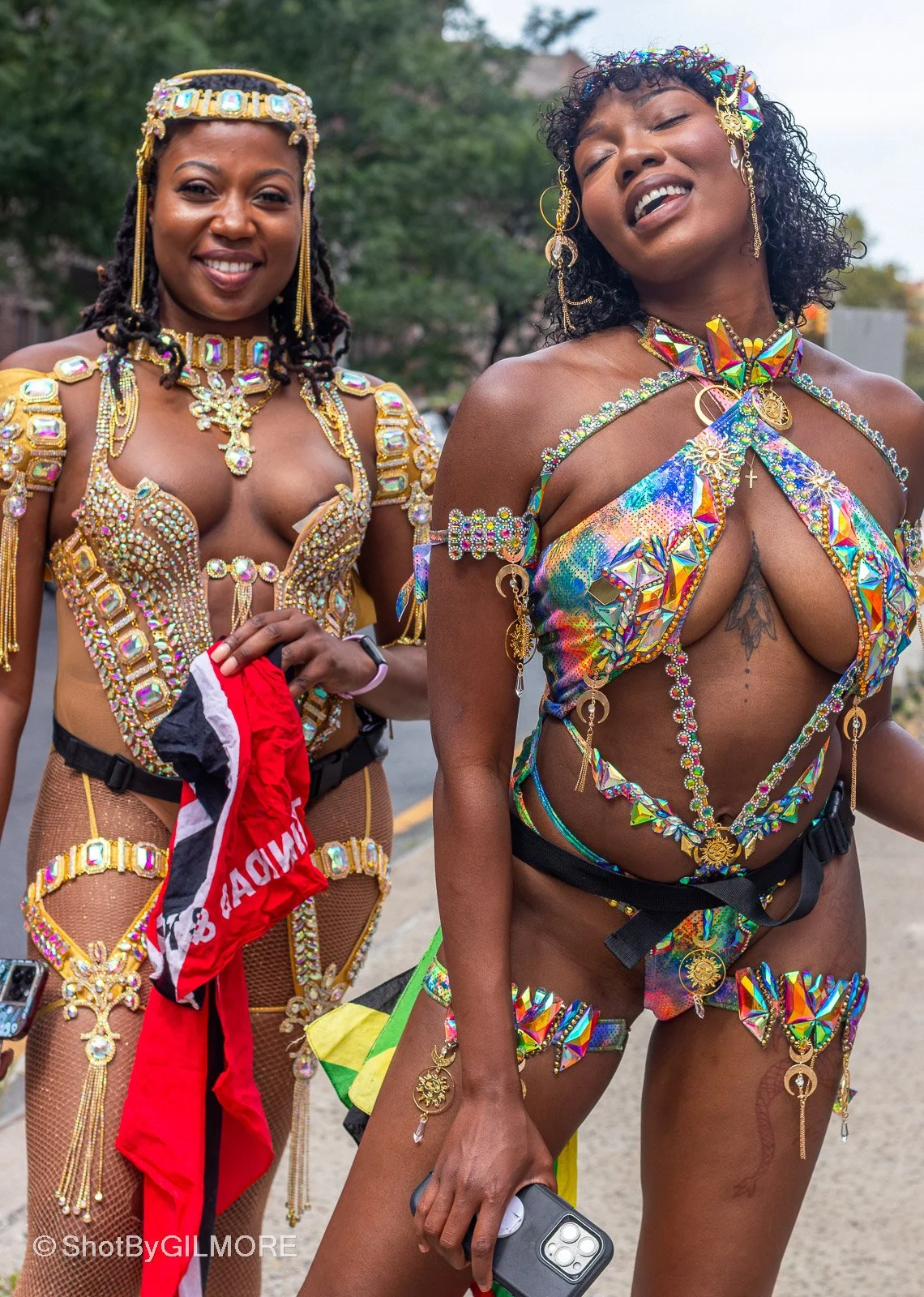 Two women dressed in colorful, jeweled costumes with intricate beadwork and metallic embellishments, standing outdoors during a celebration or parade.
