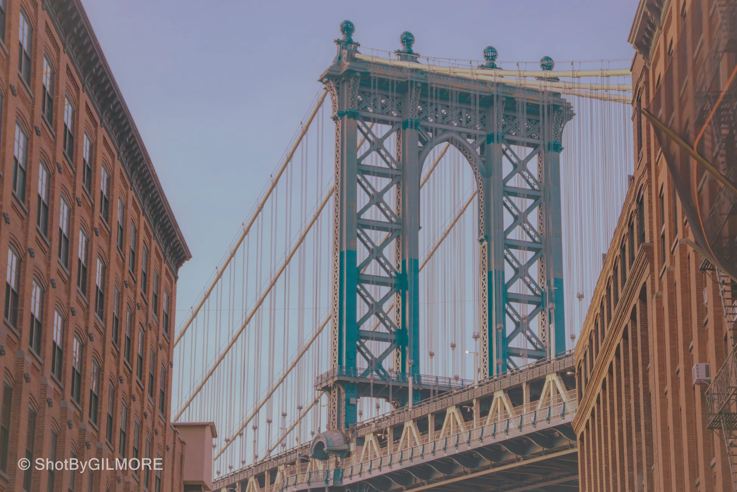 View of the Brooklyn Bridge with the Manhattan Bridge in the background, flanked by brick buildings on both sides in New York City.