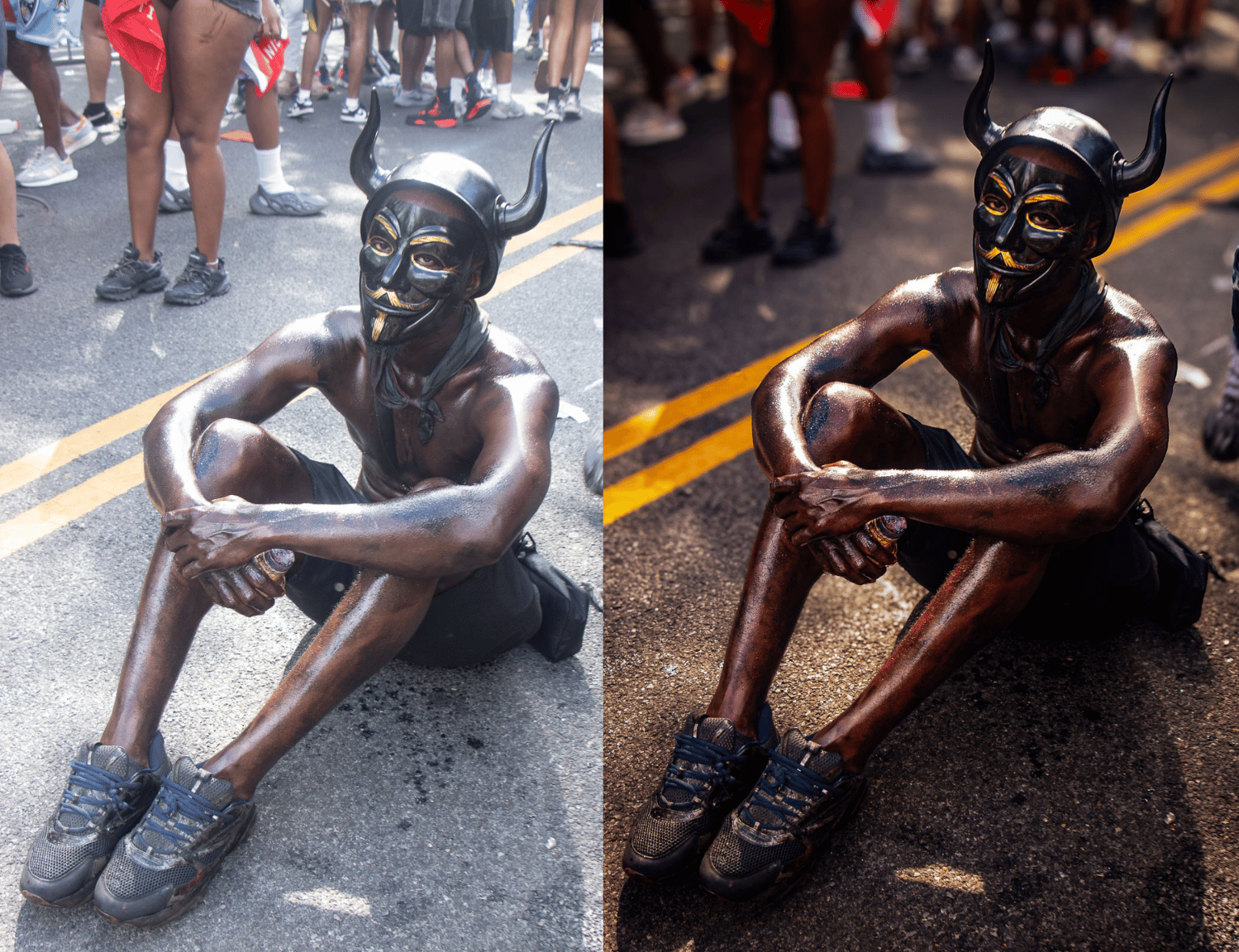 A man dressed in a devil costume with a black mask, horns, and a painted face, crouching on a street during a parade or festival, with a crowd of people in shorts and t-shirts in the background.