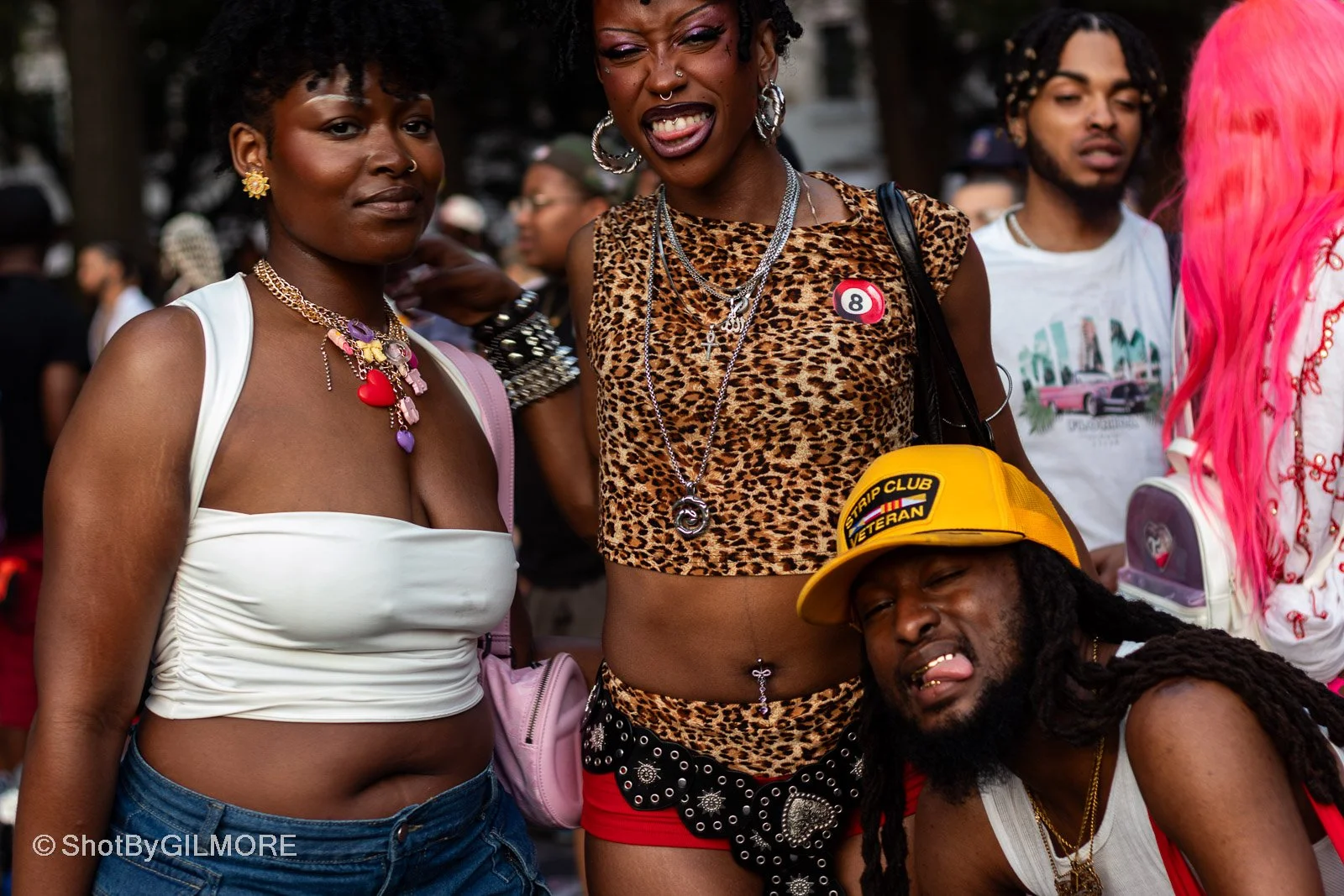 A group of people outdoors, dressed in colorful and fashionable clothing, some with accessories, with trees in the background.