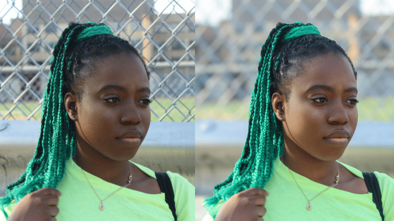 A young woman with green and black braided hair, wearing a bright green shirt and a gold necklace, standing in front of a chain-link fence outdoors.