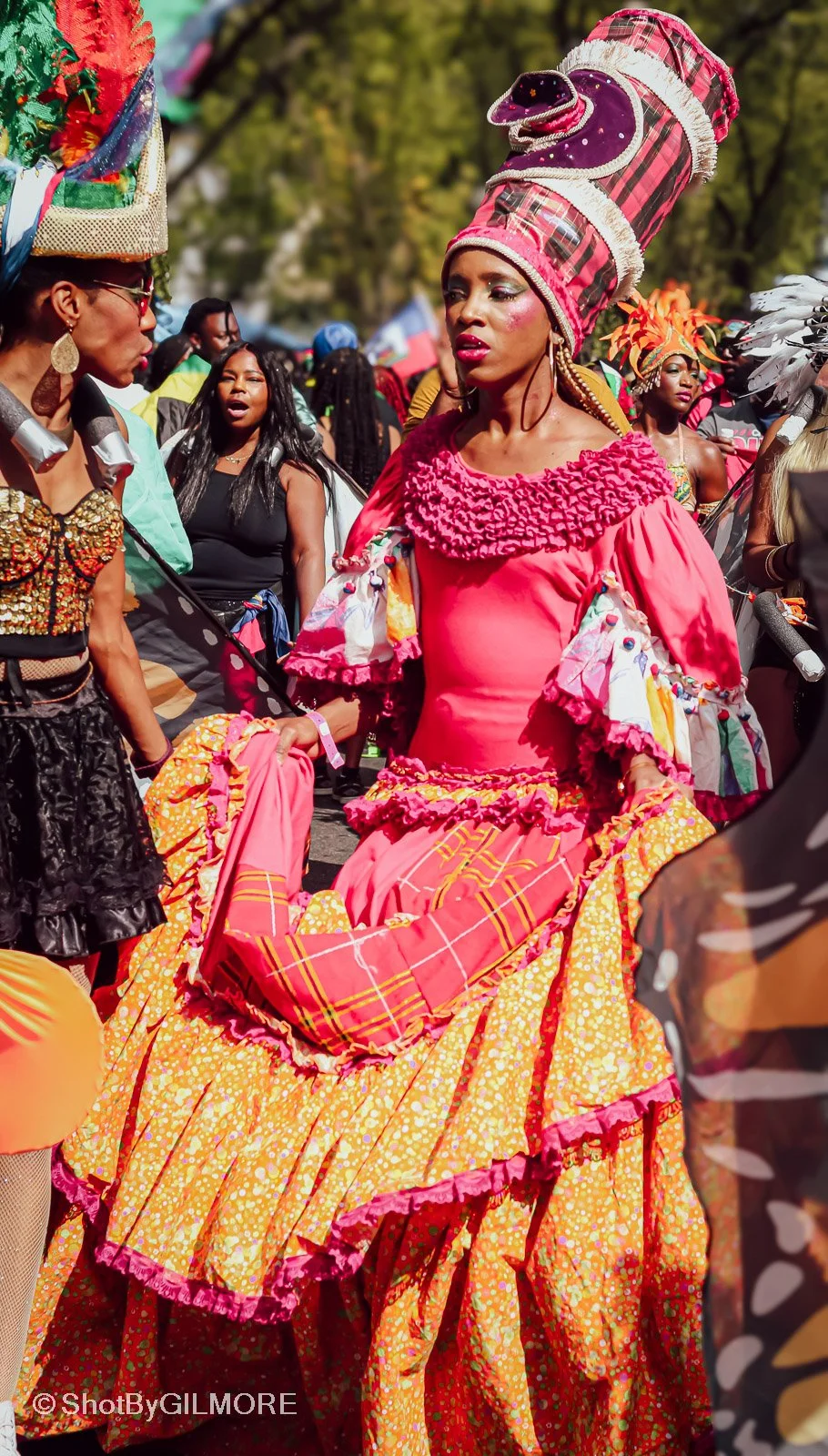 Women dressed in colorful, elaborate costumes, participating in a cultural parade or festival outdoors.