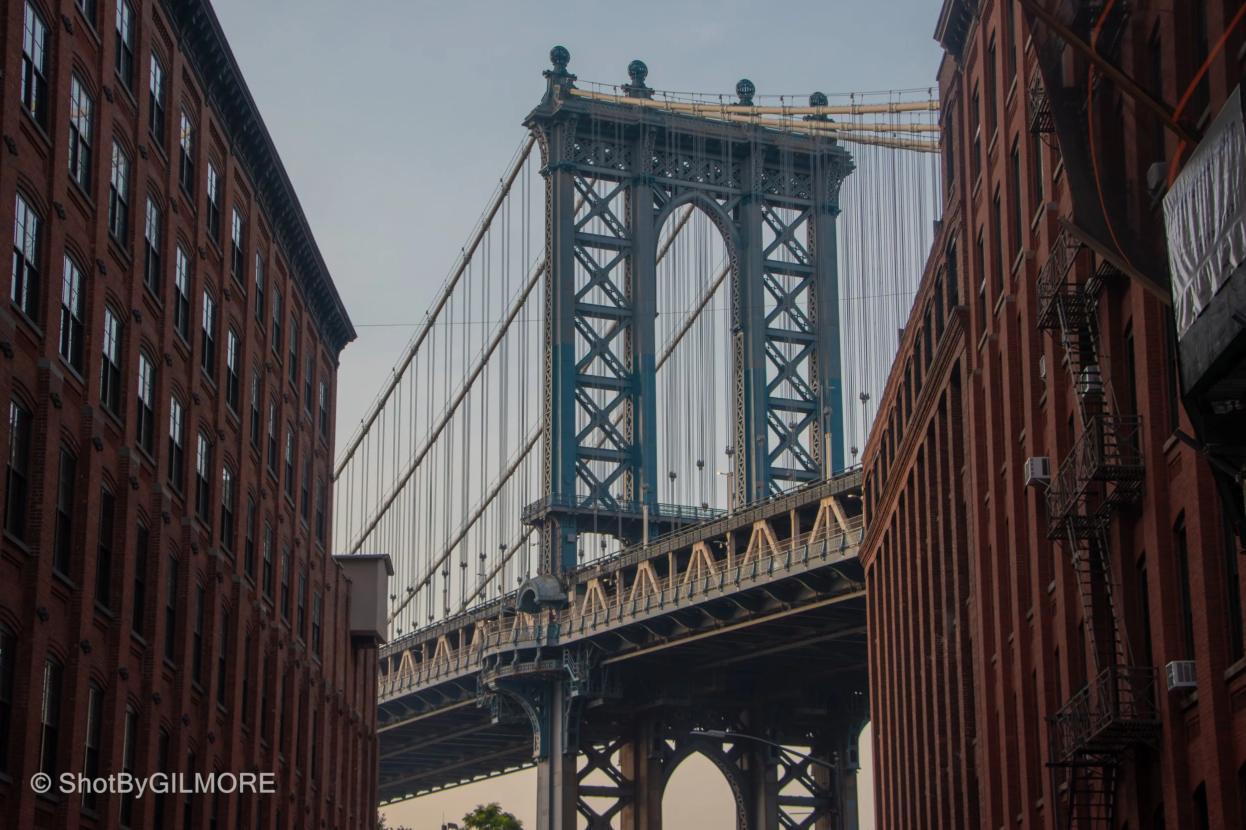 View of the Brooklyn Bridge in New York City seen through two red brick buildings.