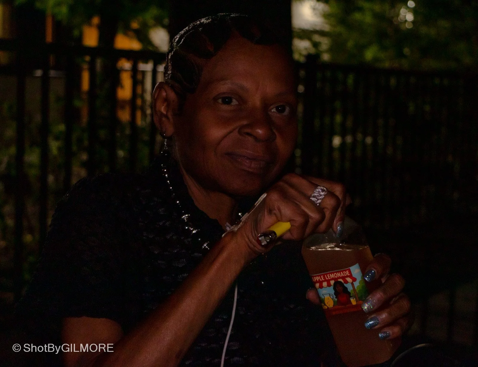 A woman holding a bottle of apple lemonade at night outdoors, with a dark background and dim lighting.