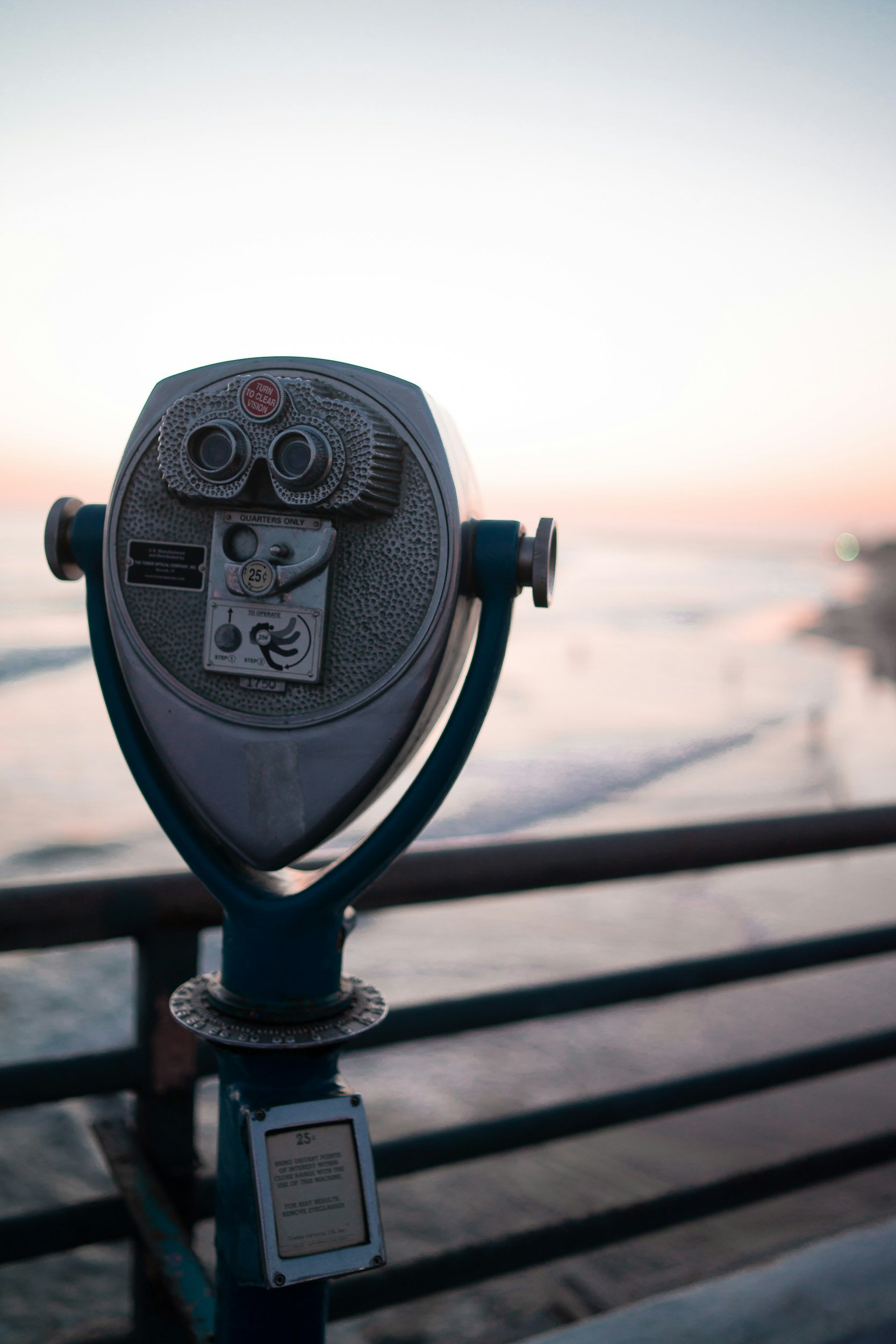 A coin-operated binocular viewer on a pier looking out toward the ocean at sunset.