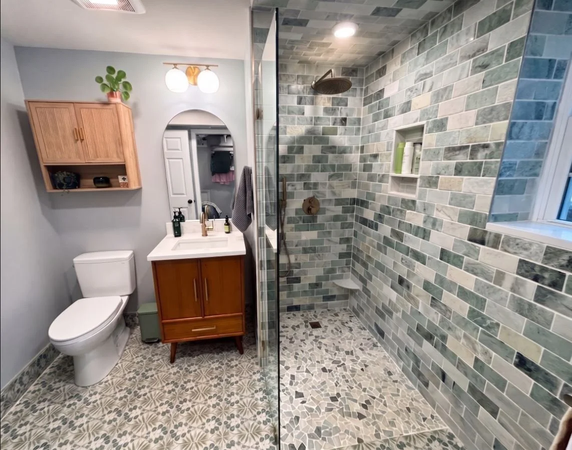 A sophisticated luxury bathroom remodel in Atlanta, GA, featuring a custom natural wood vanity, an elegant arched mirror, and matching wall-mounted cabinetry by Mahfoud Construction Inc.