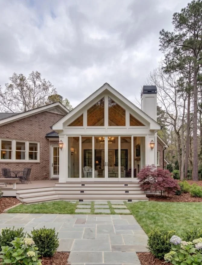 A luxury gabled-roof pavilion addition in Atlanta, GA, featuring floor-to-ceiling glass walls, a vaulted wood-plank ceiling, and a seamless connection to a traditional brick estate by Mahfoud Construction Inc.