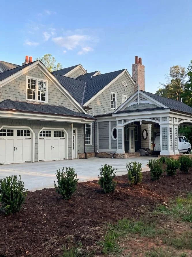 A side-view of a luxury custom home in Atlanta, GA, featuring matching carriage-style garage doors and premium architectural siding by Mahfoud Construction Inc.