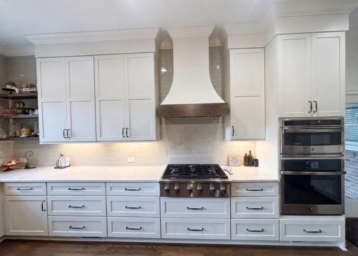 A bright, luxury kitchen remodel in Atlanta, GA, featuring floor-to-ceiling white shaker cabinets, a custom wood-trimmed vent hood, and professional-grade stainless steel appliances by Mahfoud Construction Inc.