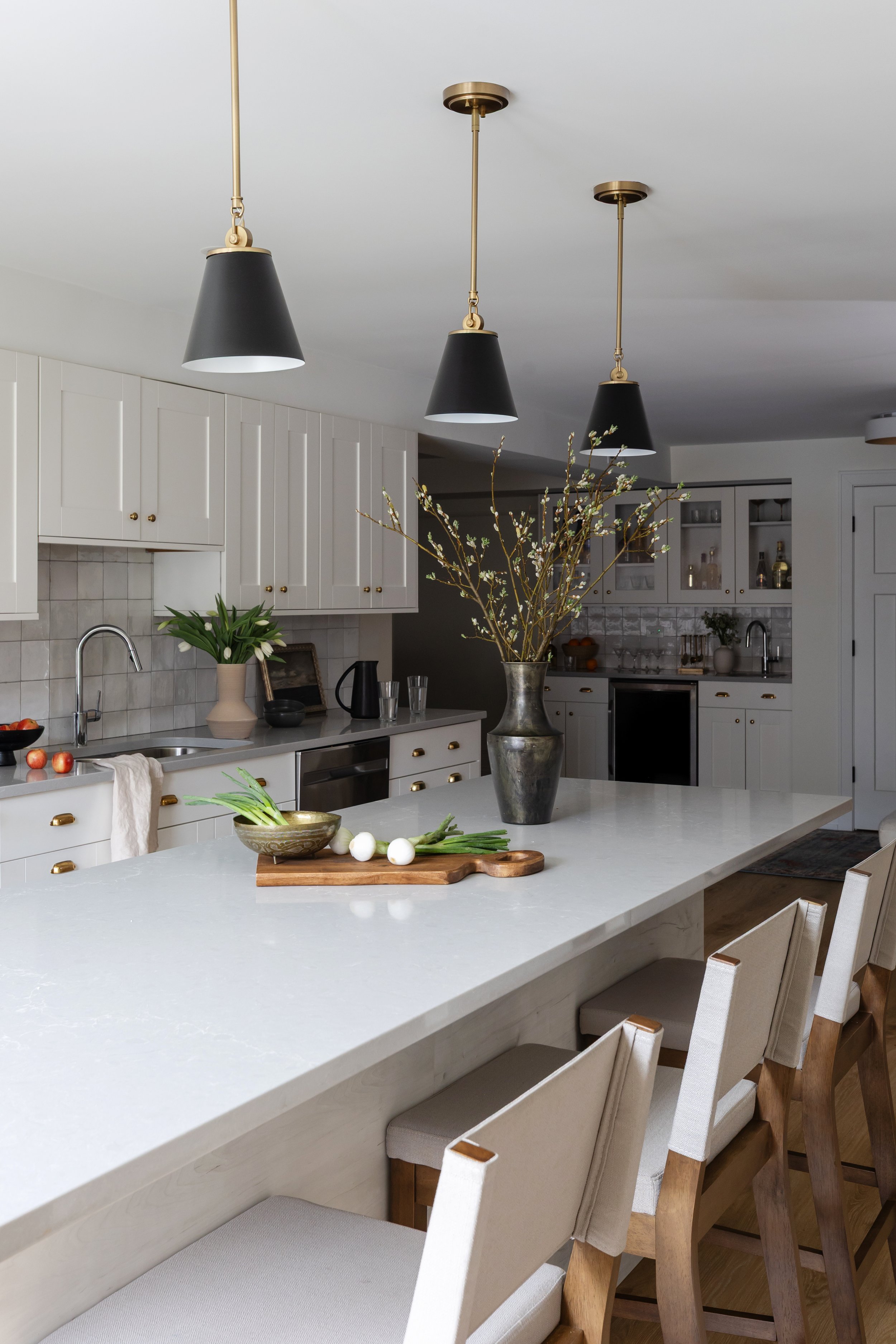 Modern kitchen with white cabinetry, a large marble island, black pendant lights, and a vase with branches as decor.