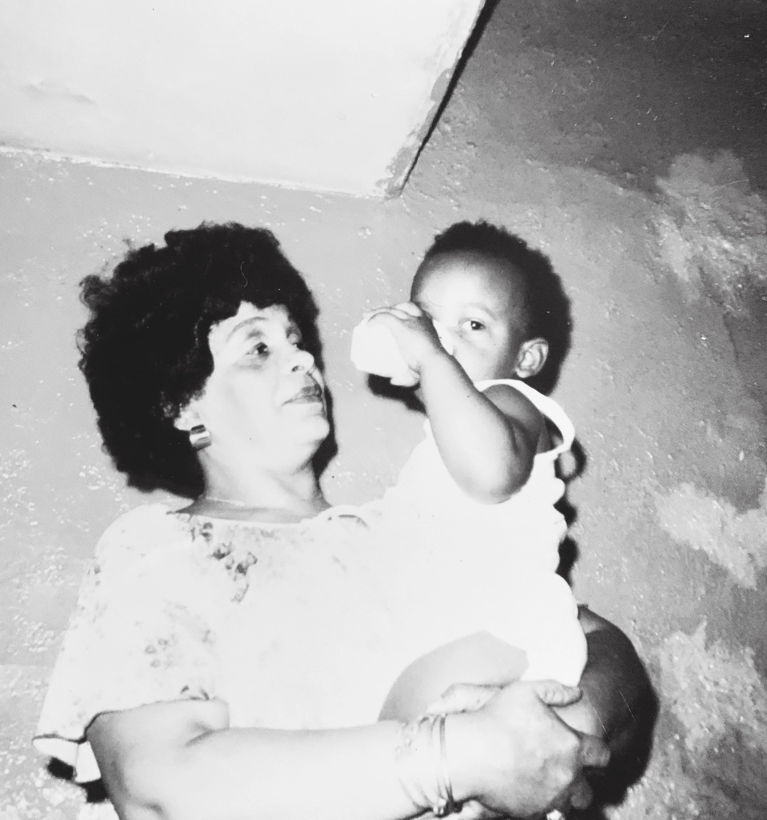 Two children lying on the ground outdoors, looking up, with a corner of a house or building in the background.
