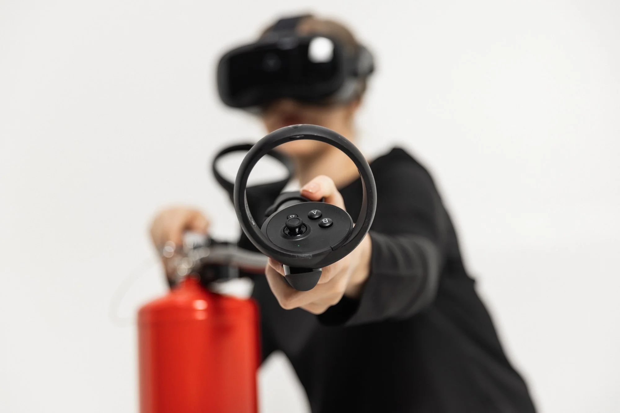 Person som bruker VR-headset og peker med en hånd, med fokus på en håndkontroller. Rød brannslukker er i forgrunnen.