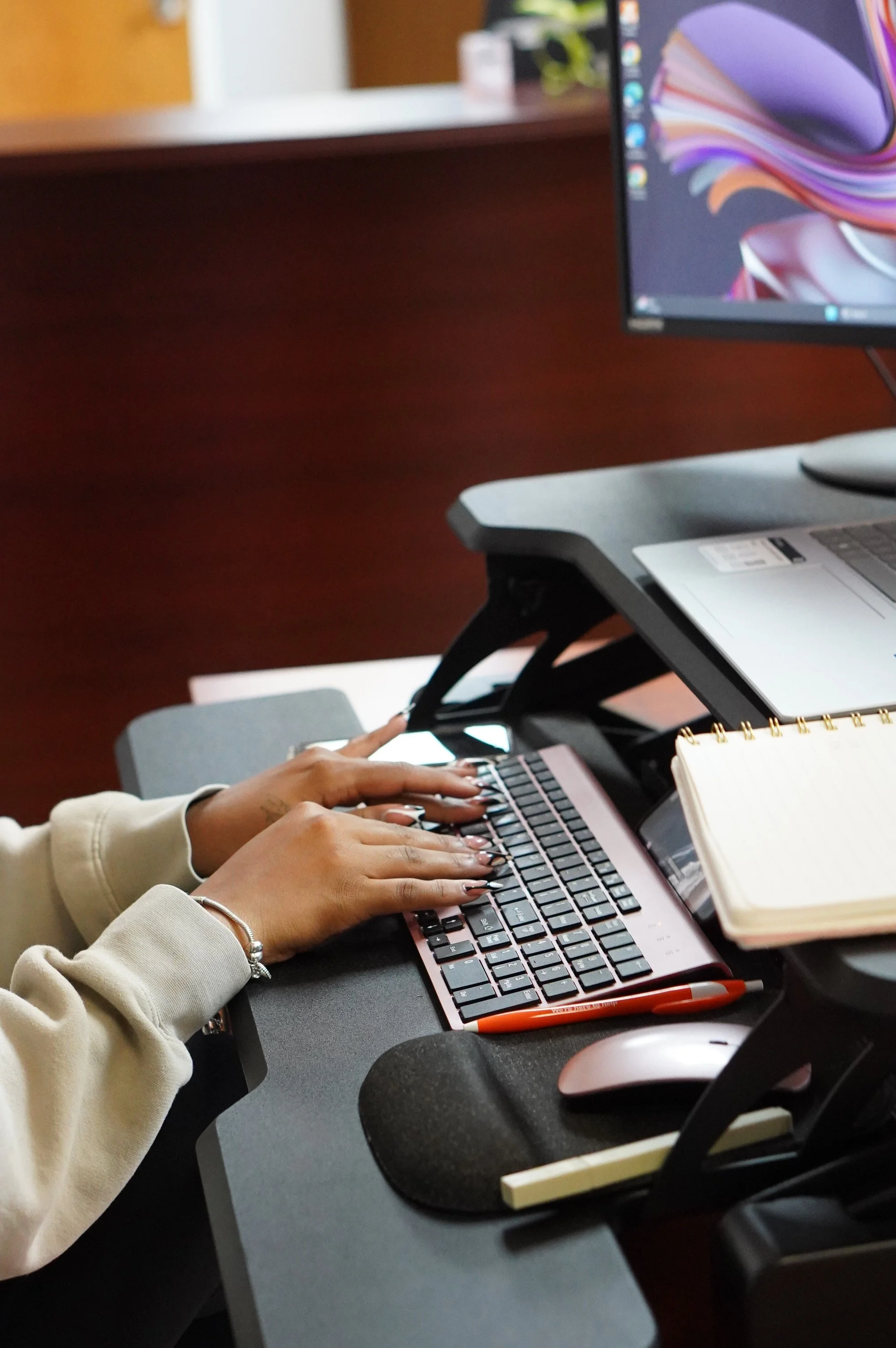 A person typing on a laptop at a desk with a smartphone, notebook, and mouse.