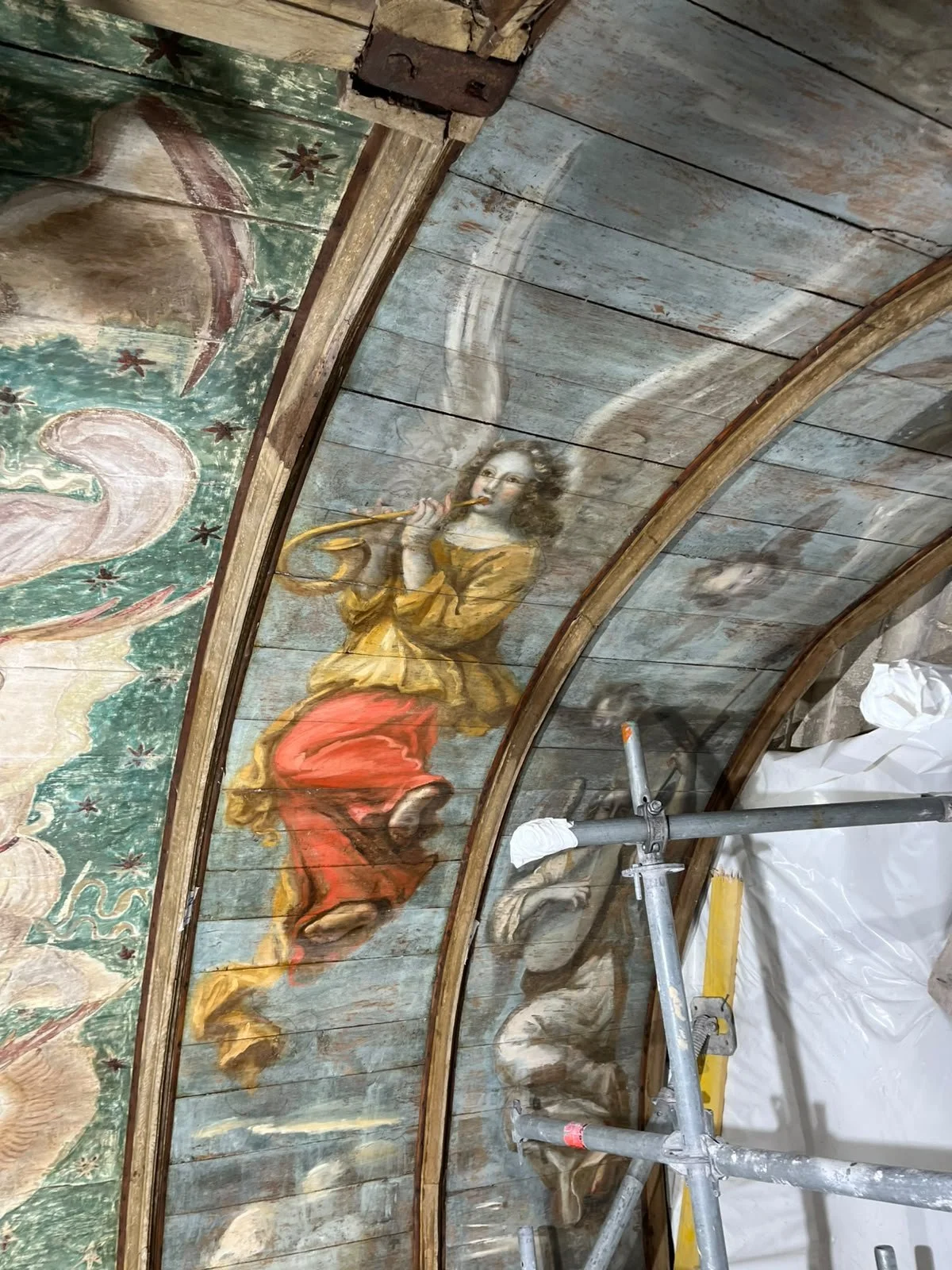 Peinture religieuse d'un ange avec un instrument à vent sur un plafond en bois, en cours de restauration.