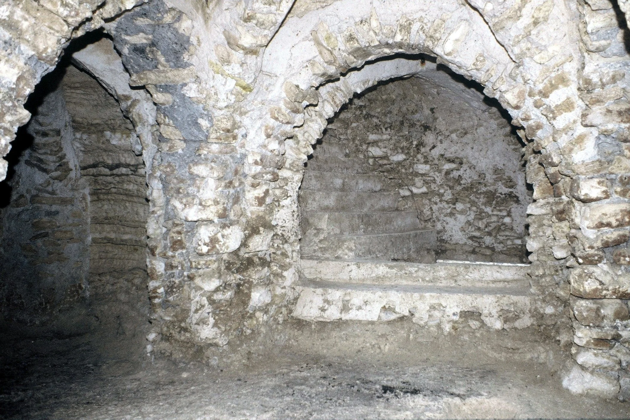 Image d'une ancienne structure en pierre avec des arches, probablement une crypte ou une cellier souterrain.