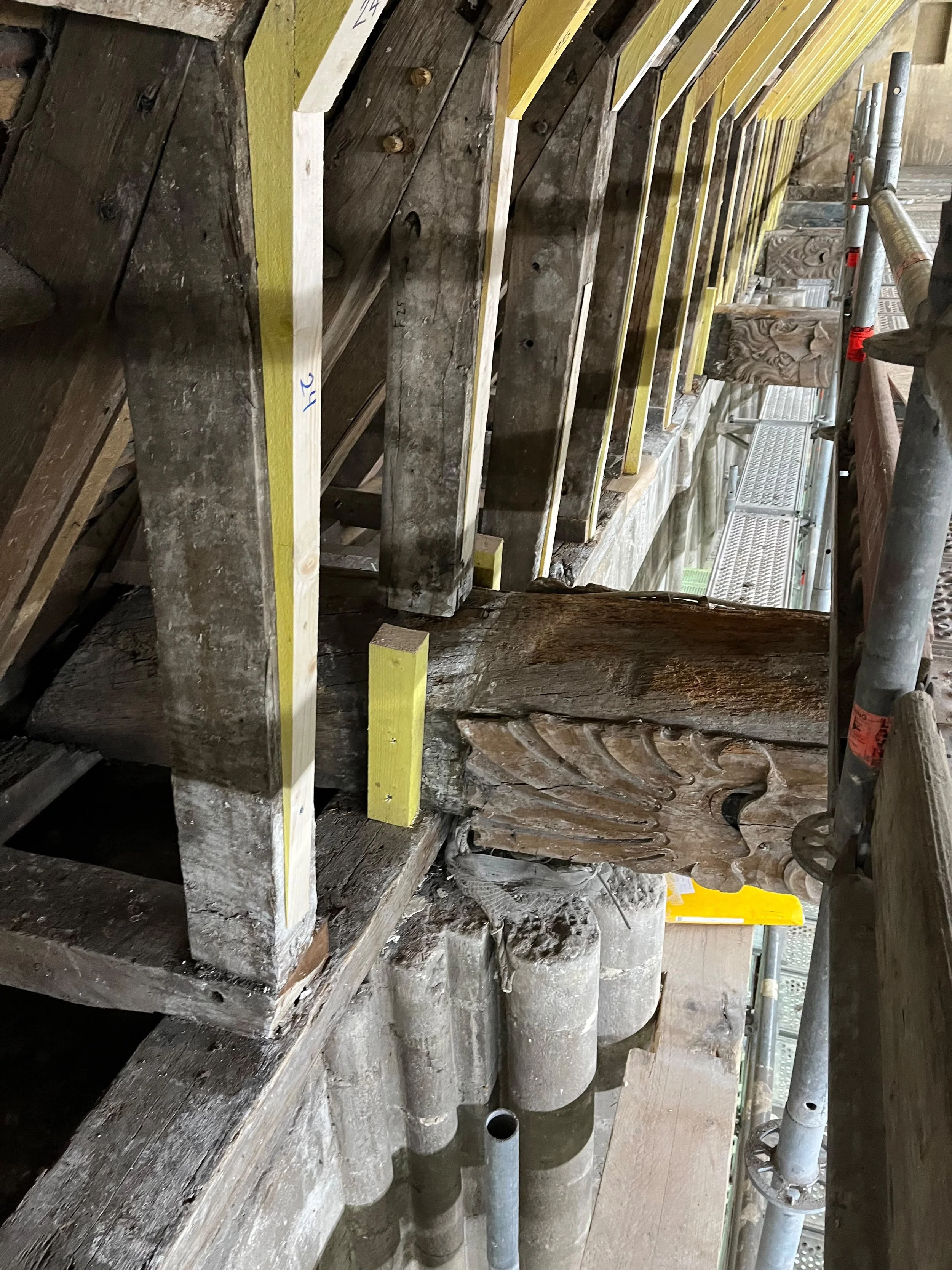 Travaux de restauration du bois et sculpture sur bois dans un bâtiment ancien, avec échafaudage en métal installé à côté.