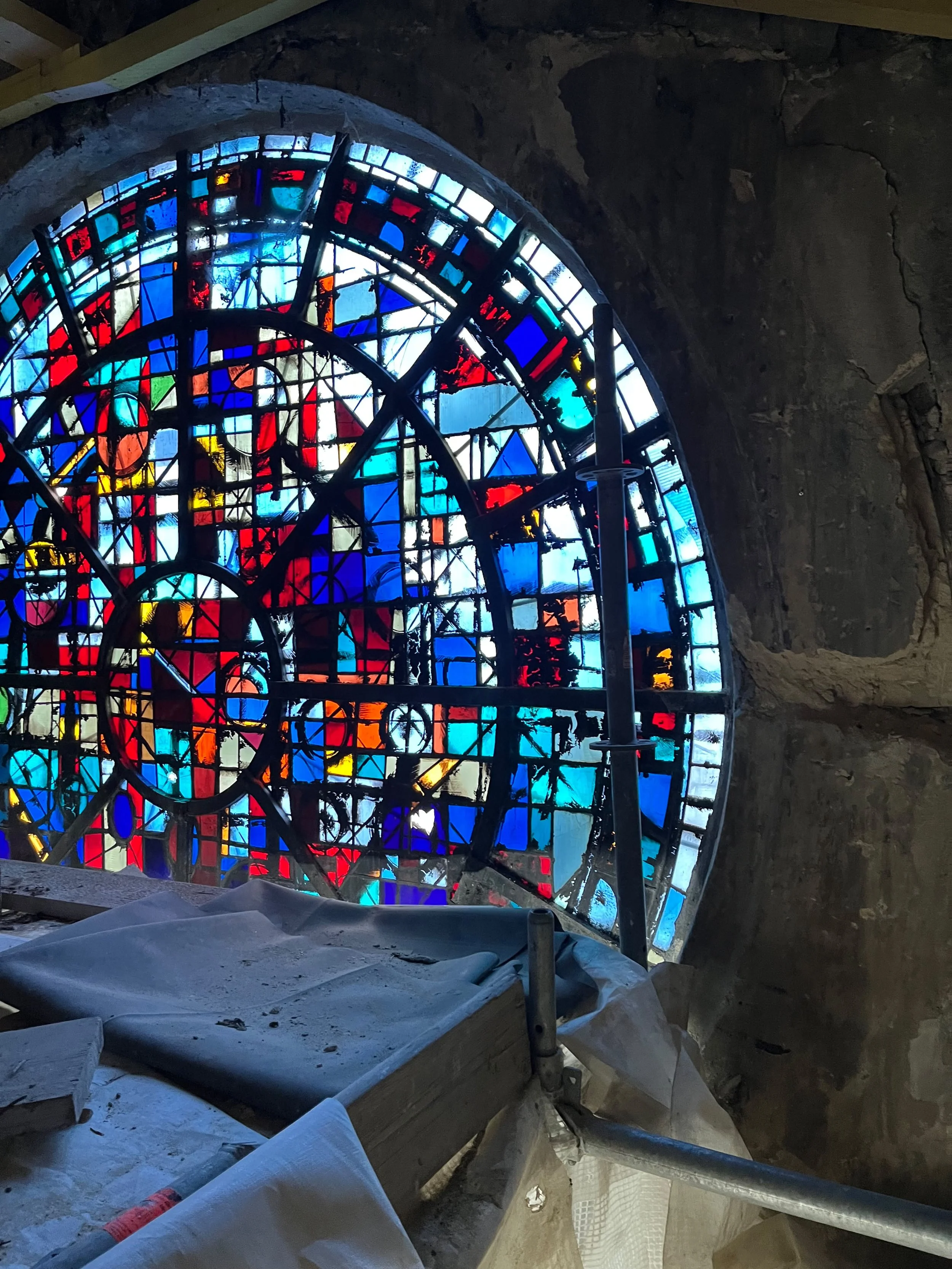 Une fenêtre de vitrail colorée en cours d'installation dans un endroit en pierre, avec des scaffolds et des matériaux de construction autour.