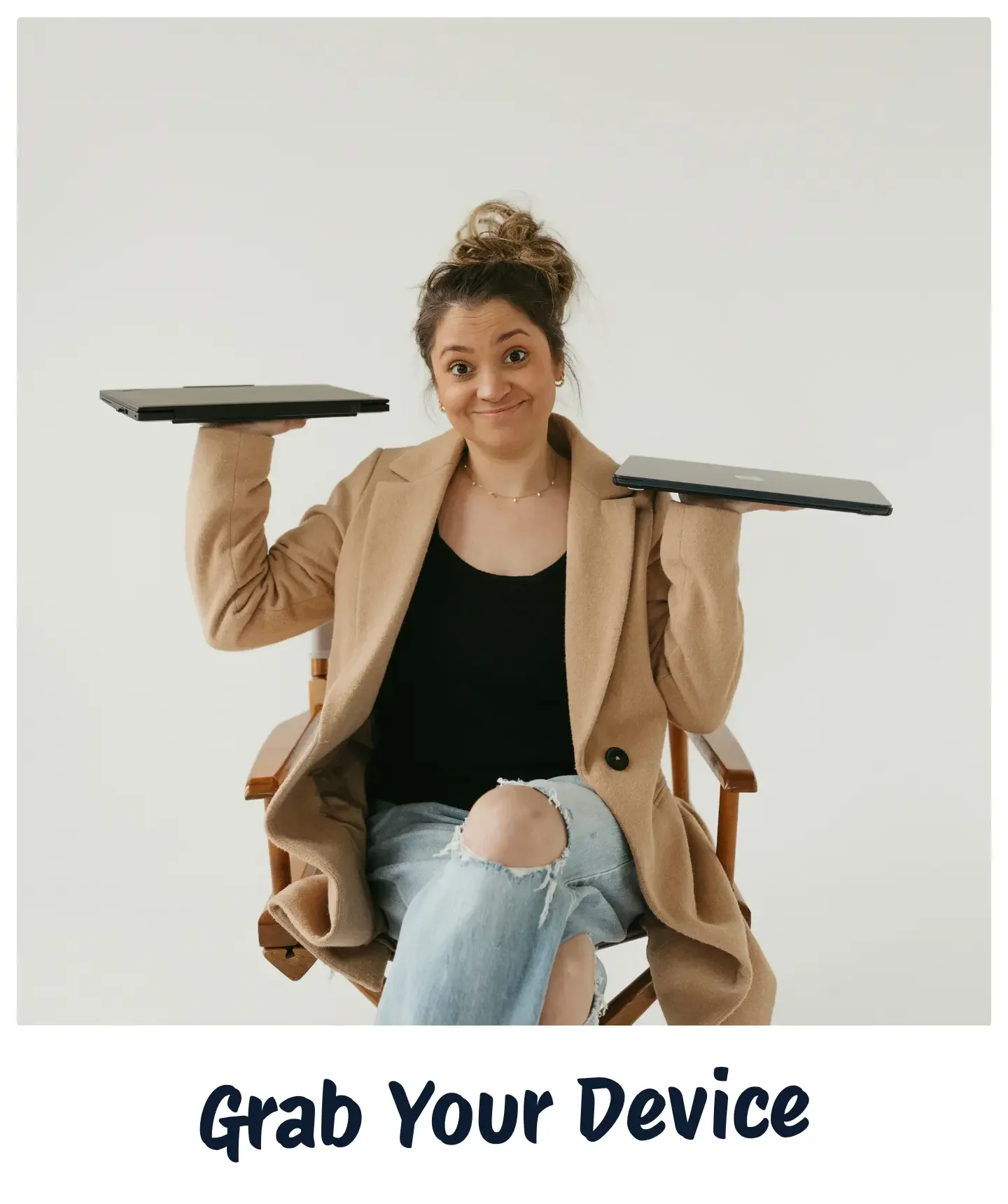 Young woman sitting in a wooden chair, holding two laptops, one in each hand, with a cheerful expression, wearing a tan coat, black top, and ripped jeans, against a white background.