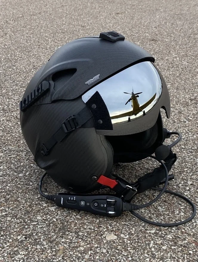 A motorcycle helmet with a reflective visor showing a helicopter and sky. Attached communication device on the helmet with wires.