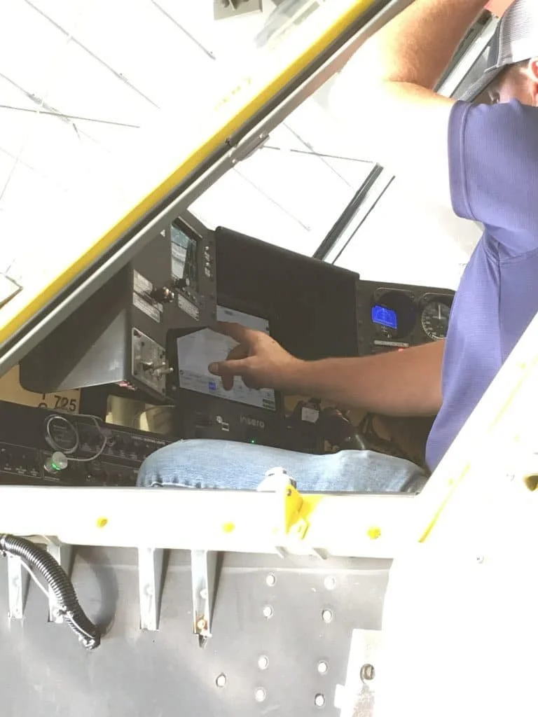 Pilot sitting in the cockpit of a small aircraft, operating instruments and controls.