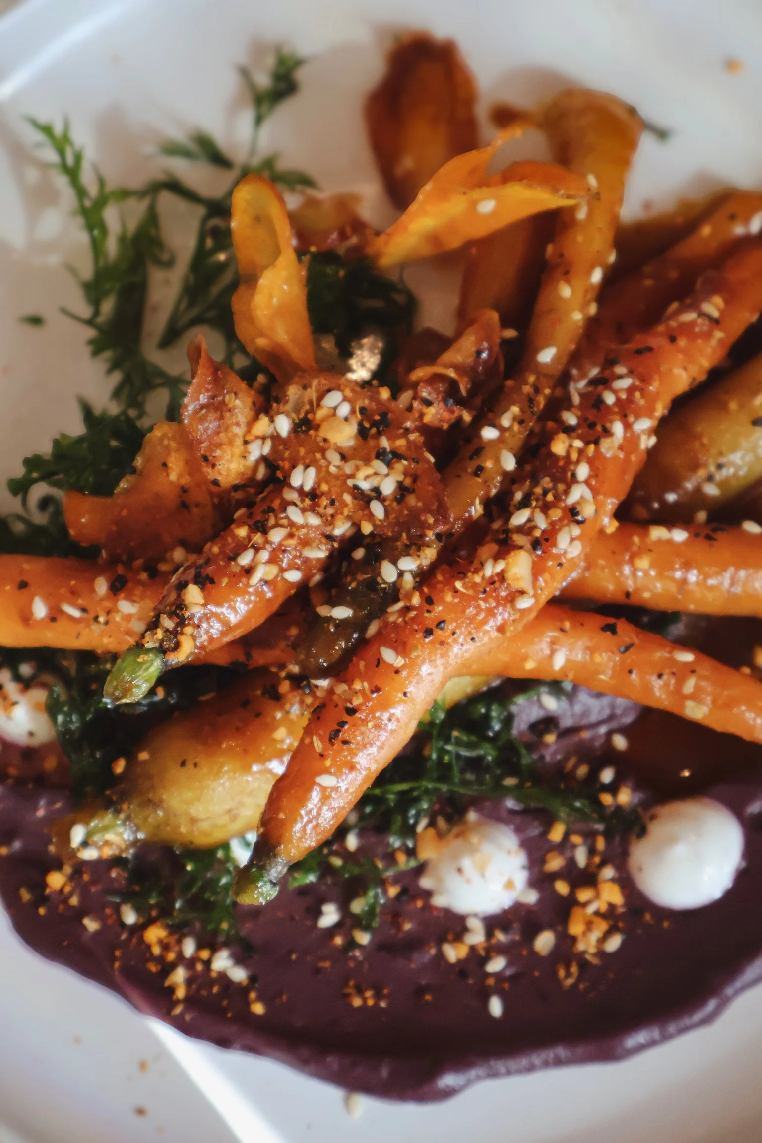 Roasted carrots with sesame seeds and a dark sauce at the bottom, garnished with herbs.