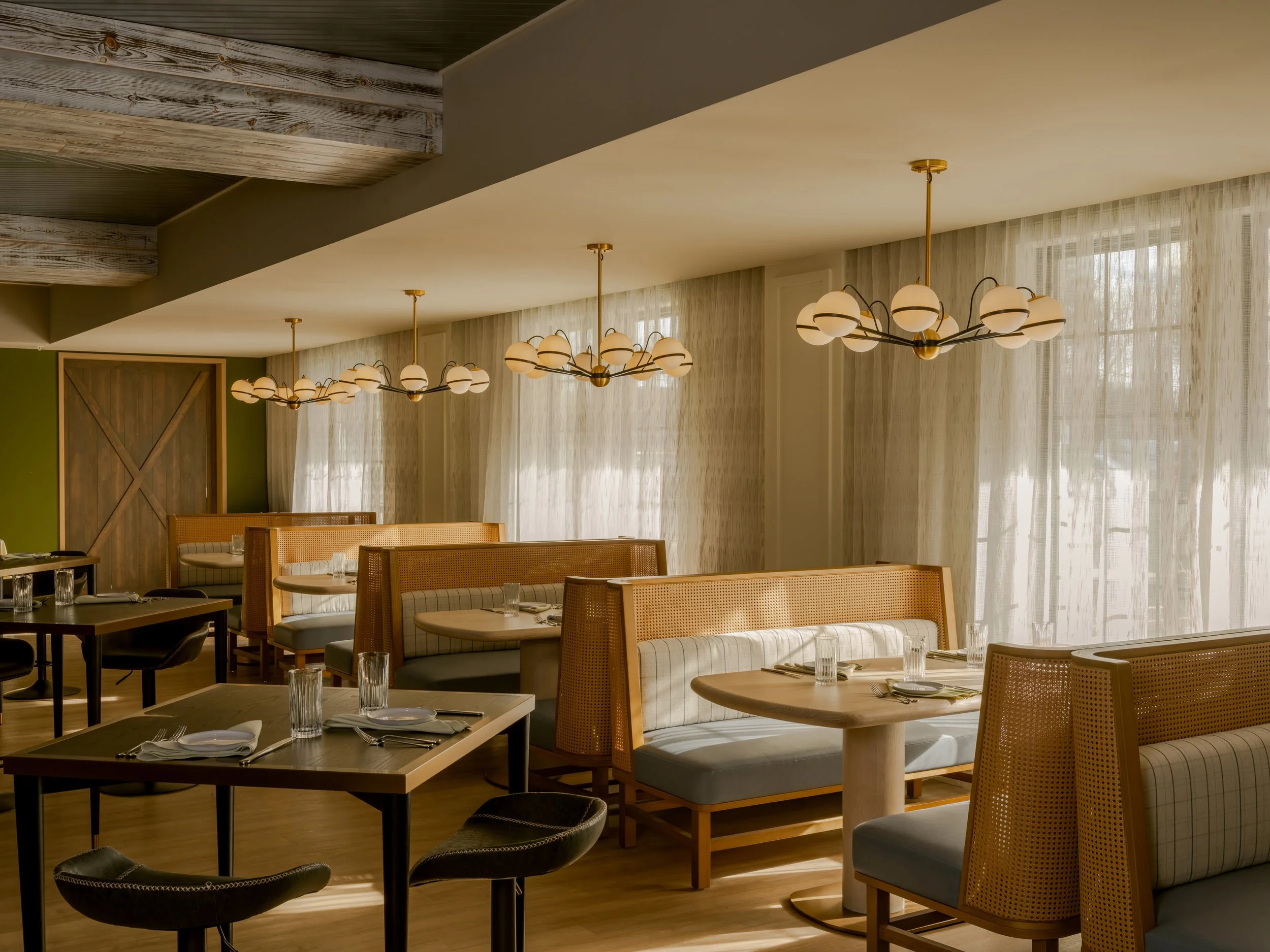 Modern dining area with round tables, cushioned chairs, and contemporary chandeliers, decorated with sheer curtains and wooden accents.