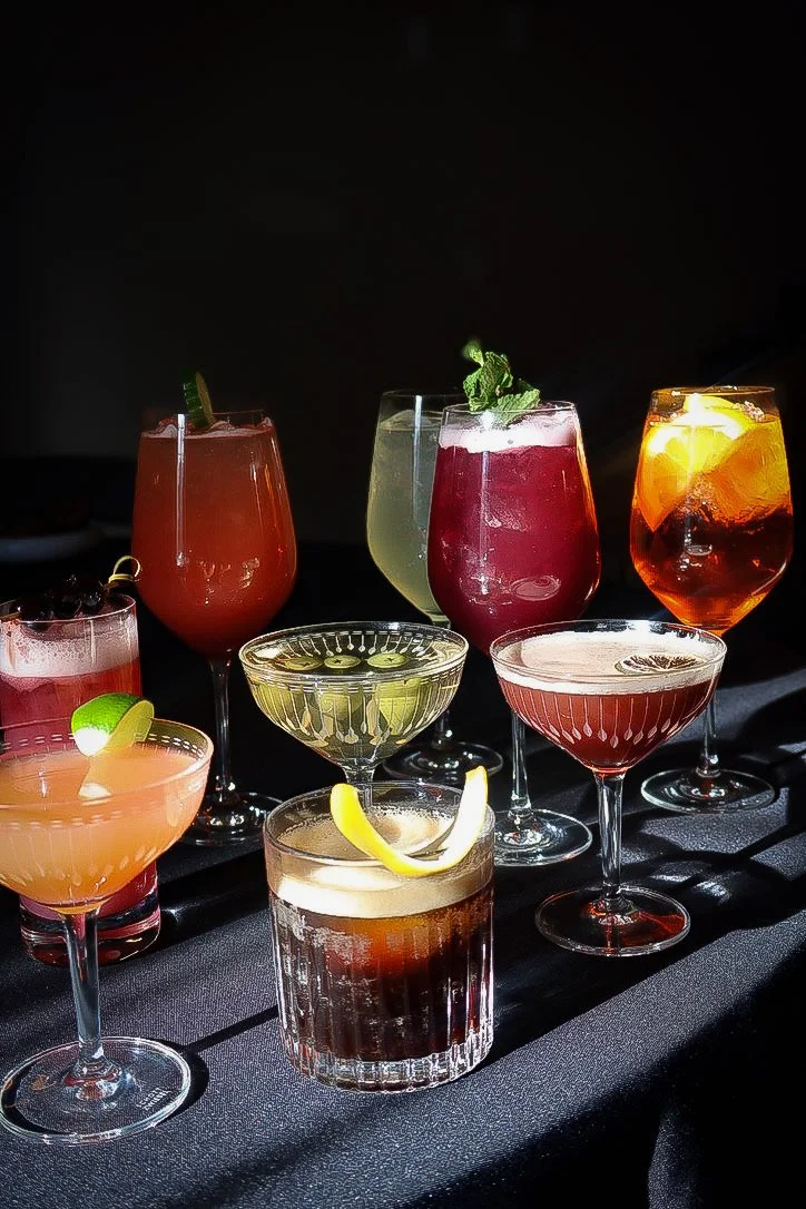 A variety of colorful cocktails on a black surface against a dark background.