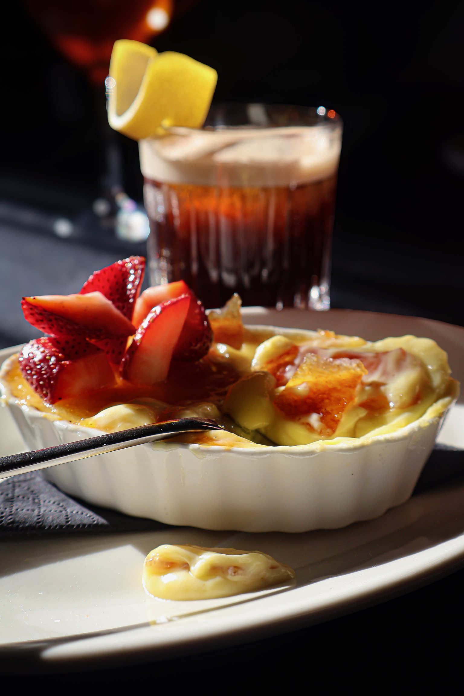 A bowl of baked Italian pasta with melted cheese, topped with sliced strawberries, served on a white plate with a silver spoon.