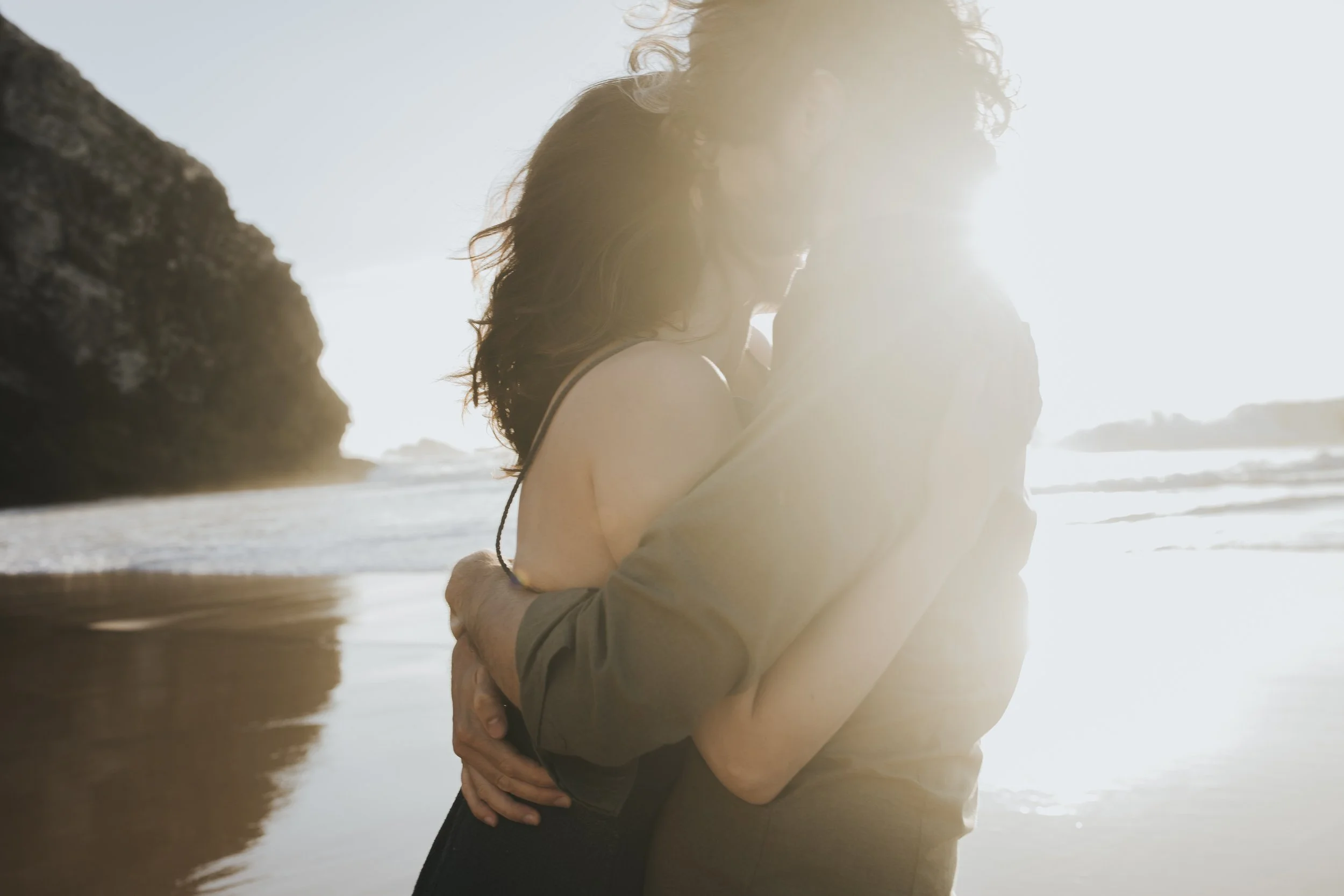 A couple embracing on a beach with the sun shining brightly in the background.