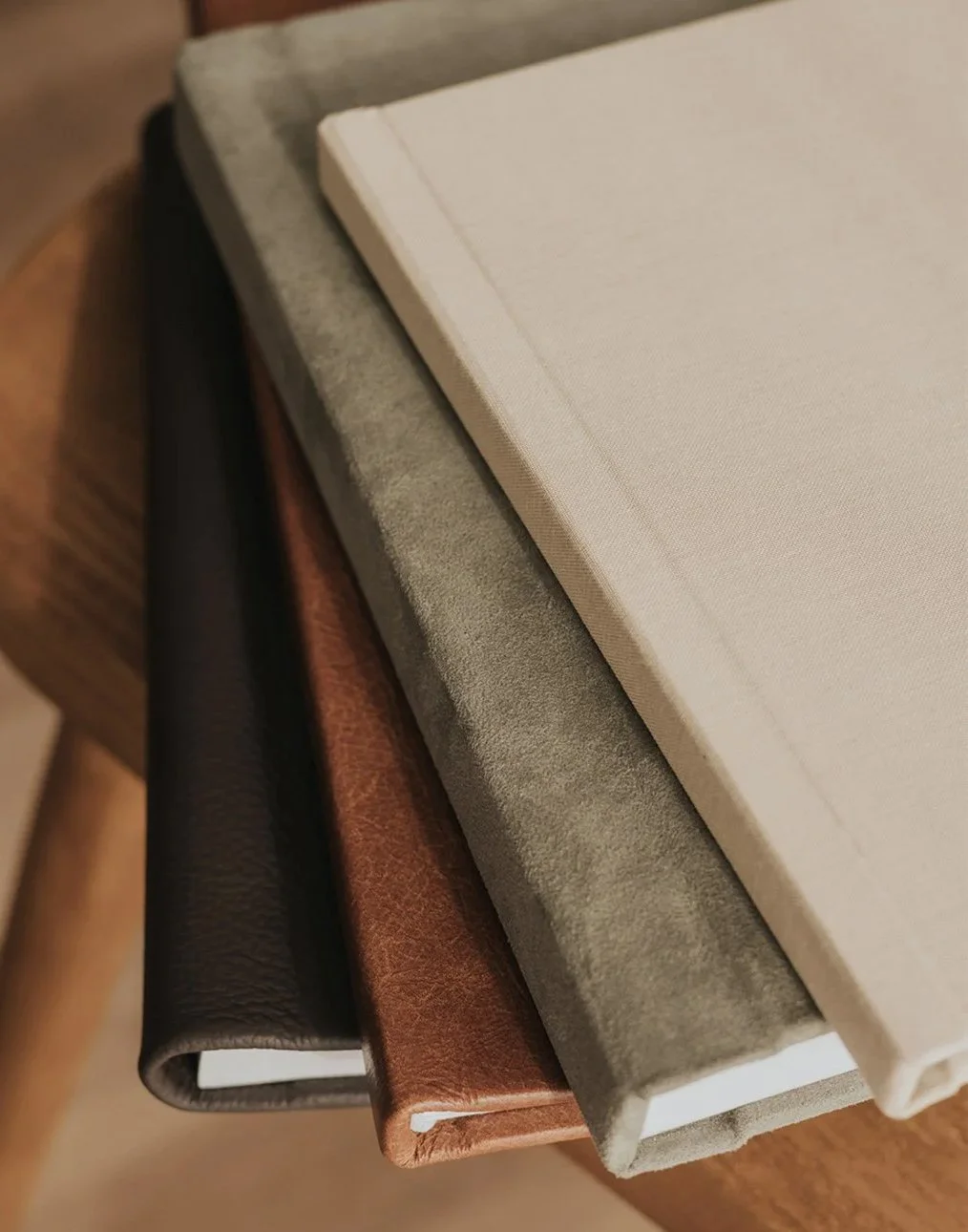 A close-up view of a stack of four notebooks with different cover textures and colors, placed on a wooden table.