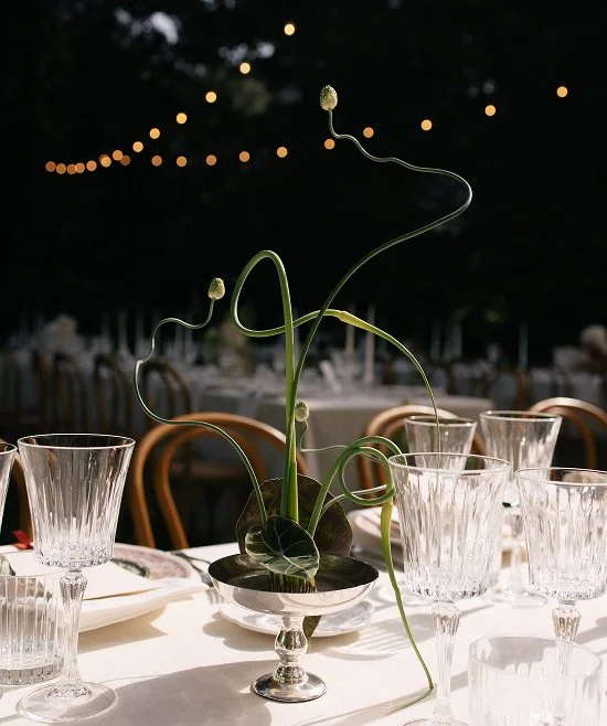 Elegant table setting with a floral centerpiece, crystal glasses, and a dark outdoor background with string lights.