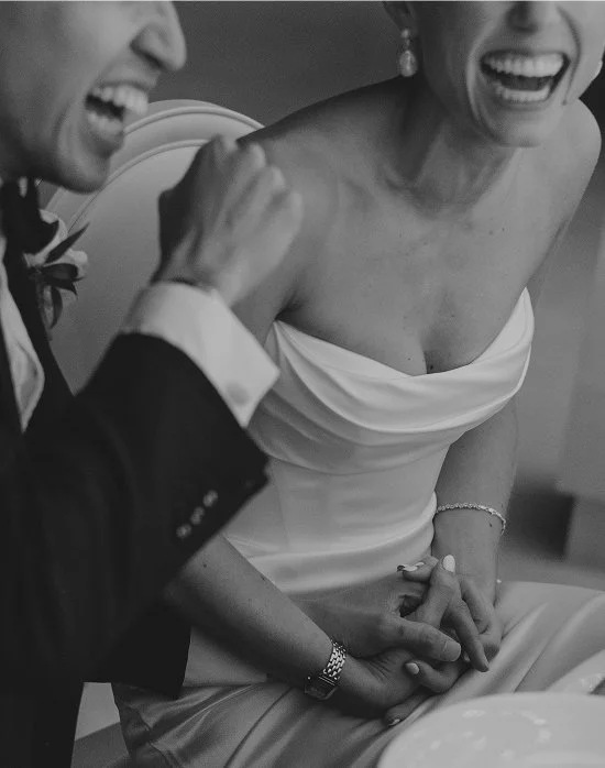 A bride and groom are laughing and holding hands, celebrating their wedding.