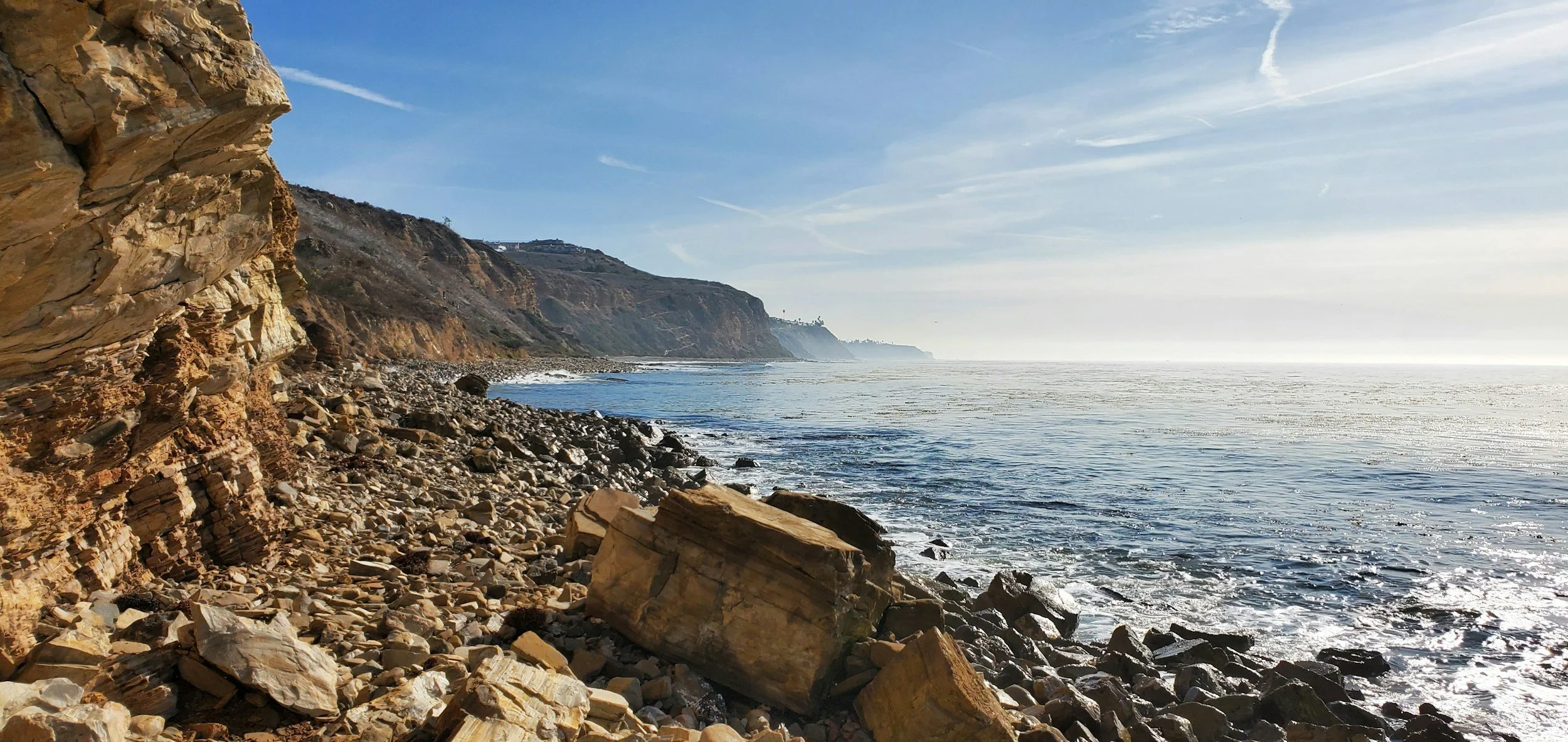 Rocky shoreline with cliffs in the distance and the ocean under a clear sky.
