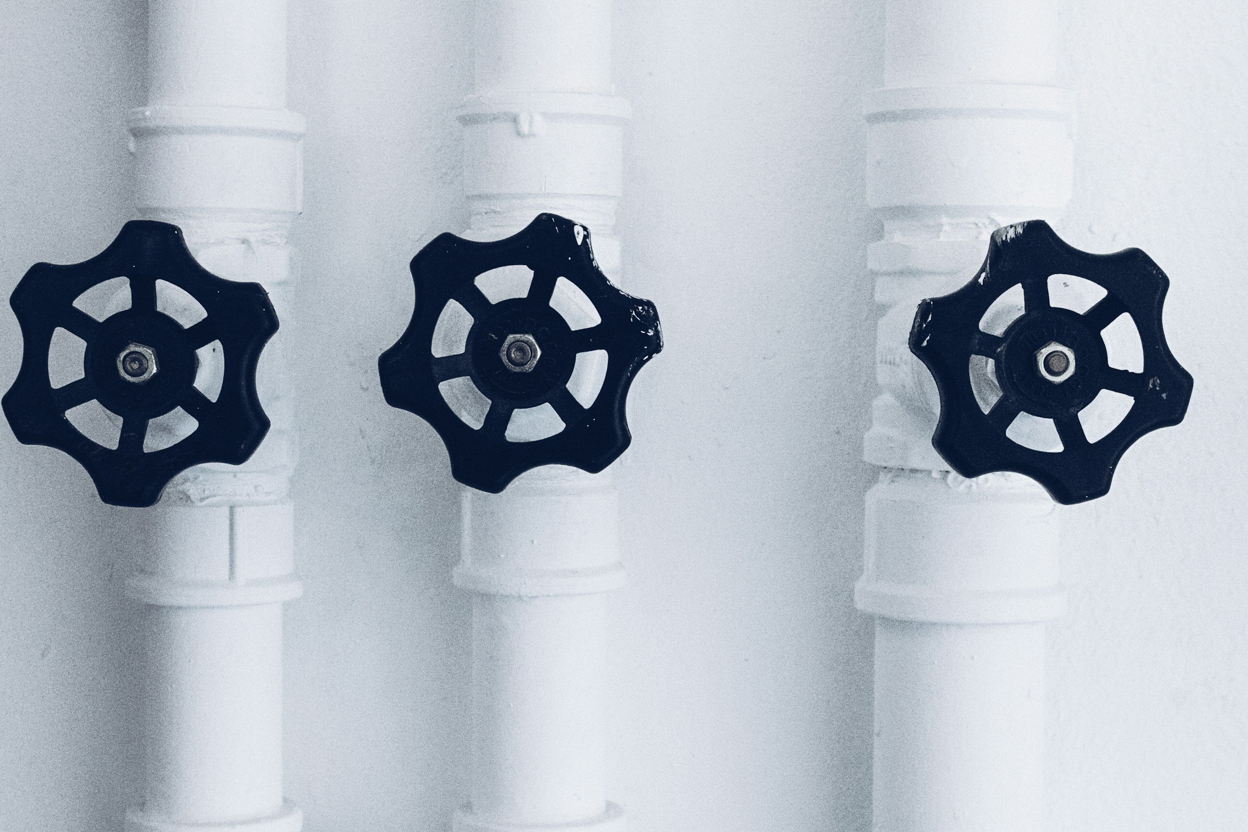 Trois robinets en plastique noir fixés sur des tubes en plastique blanc contre un mur blanc.