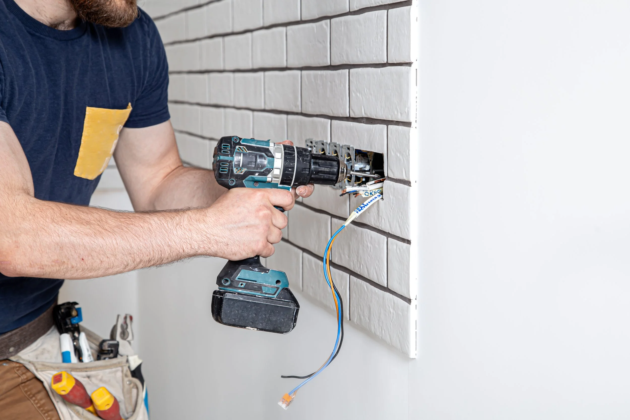 Une personne utilisant une perceuse sans fil pour effectuer des travaux électriques dans un mur en briques.